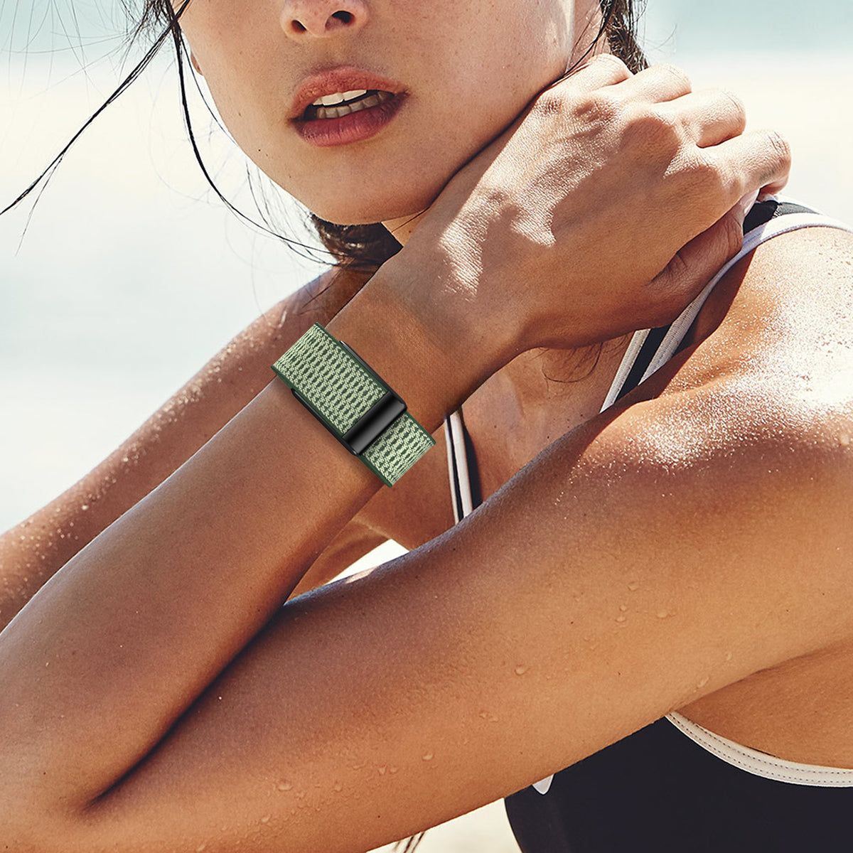 Woman wearing green knit fitness tracker strap on wrist at beach with water droplets on skin