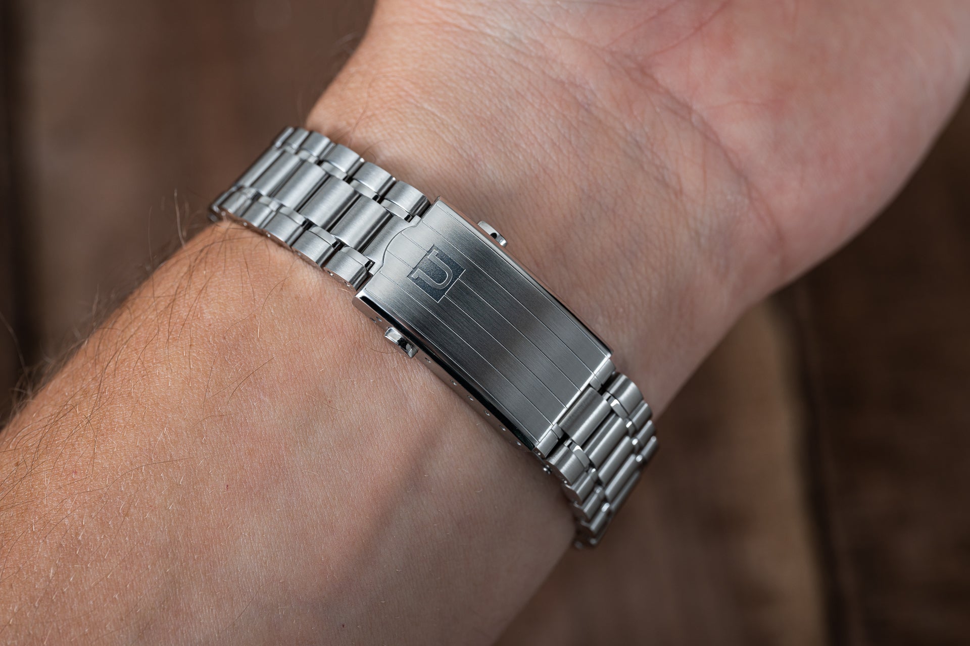 Stainless steel watch bracelet with solid link design worn on wrist, featuring brushed center links and polished edges