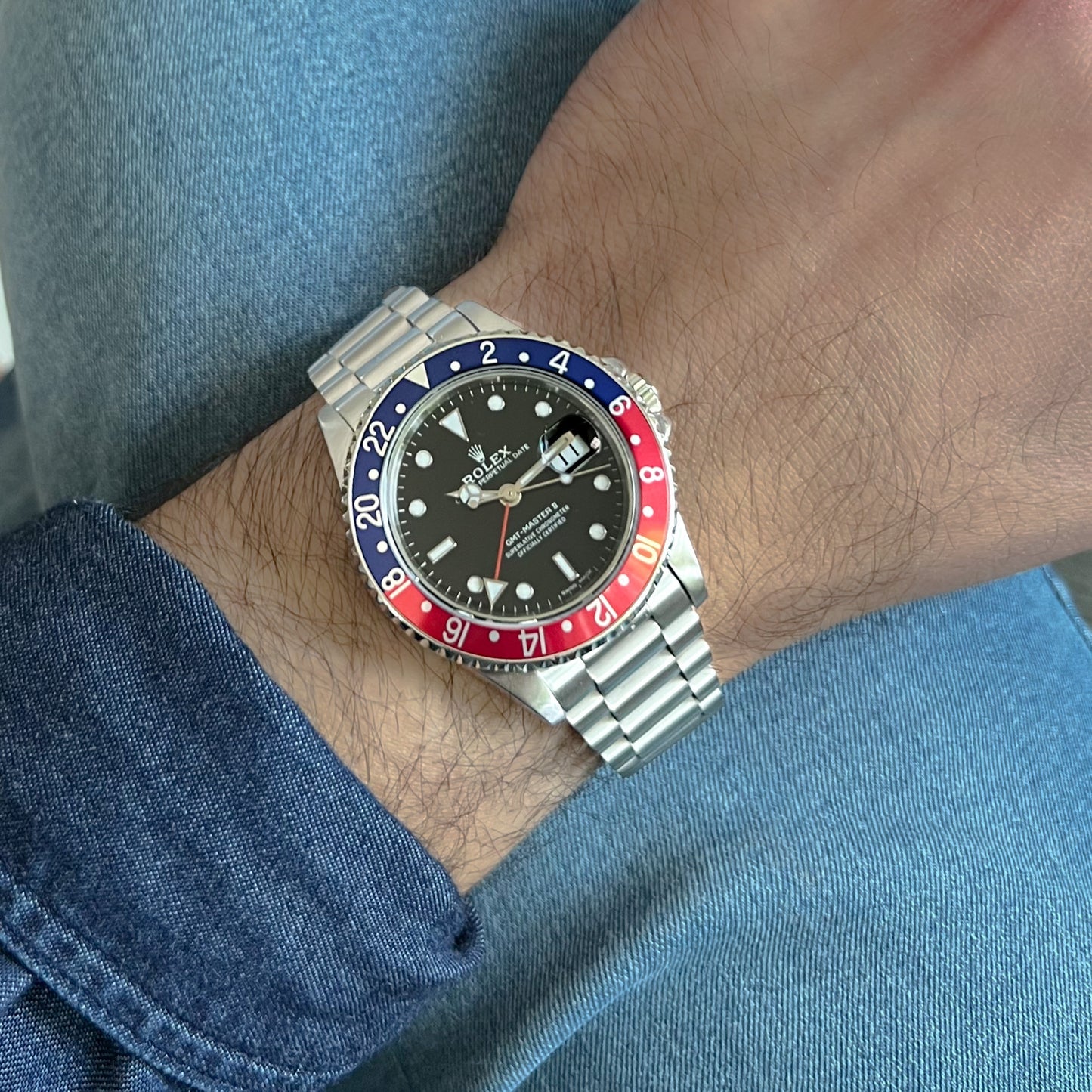 Stainless steel bracelet fitted on luxury sports watch with black dial and red-blue bezel on wrist