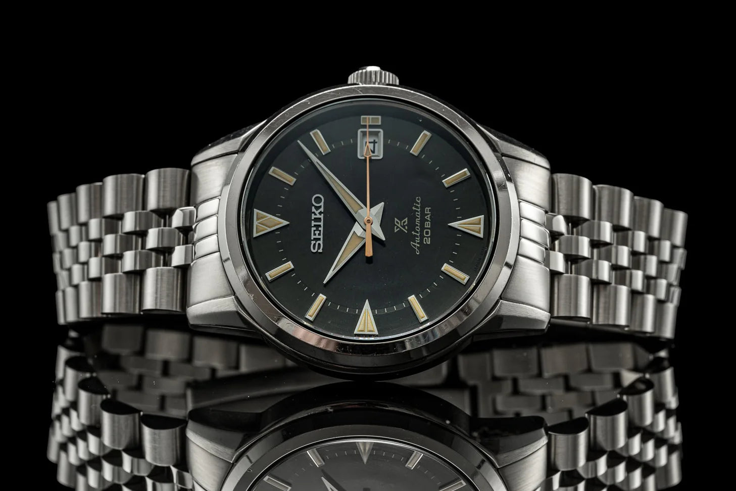 Seiko Alpinist automatic watch with black dial, gold indices, stainless steel bracelet and crown guard on black background