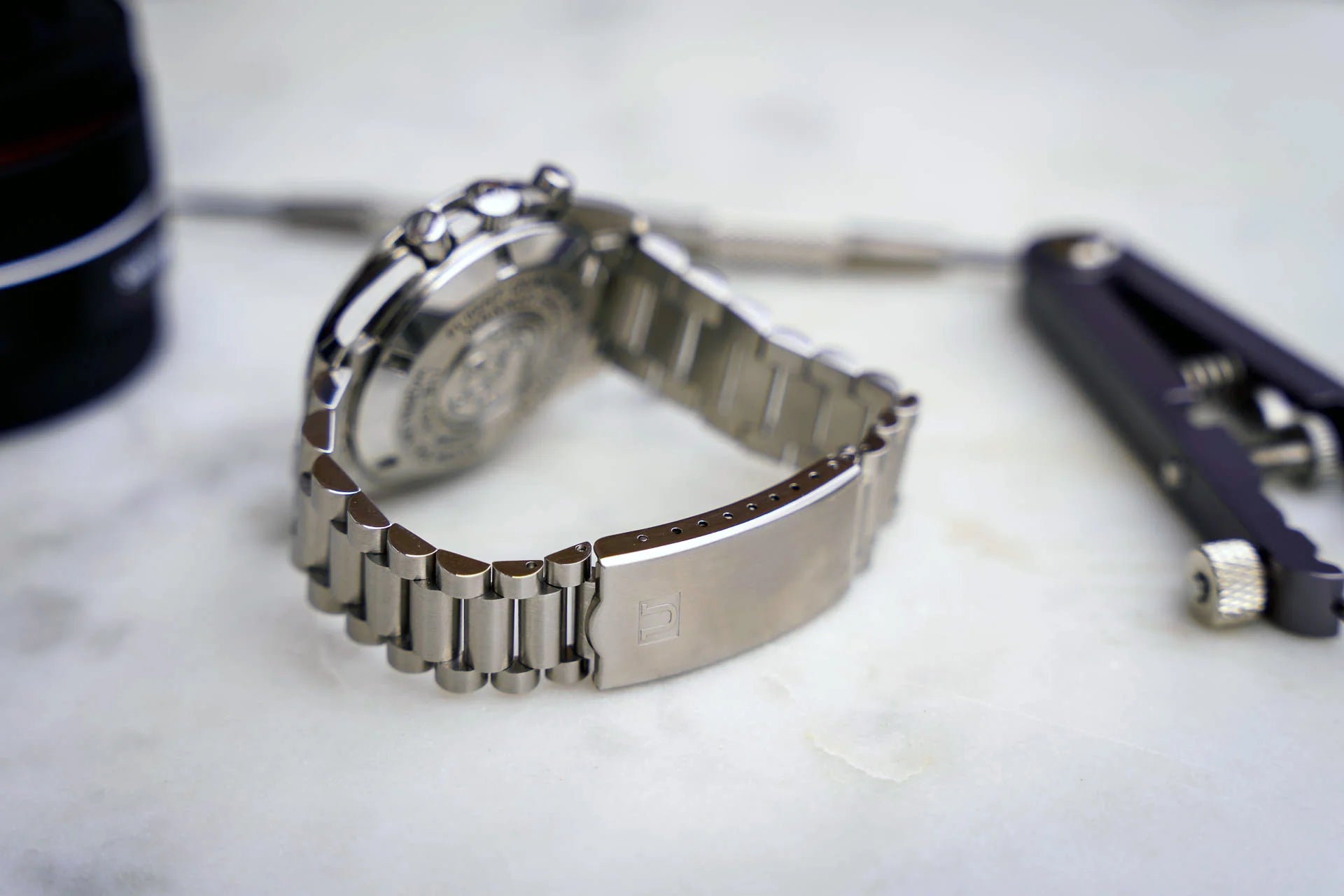 Stainless steel bracelet watch with metal link band displayed on white surface alongside accessories