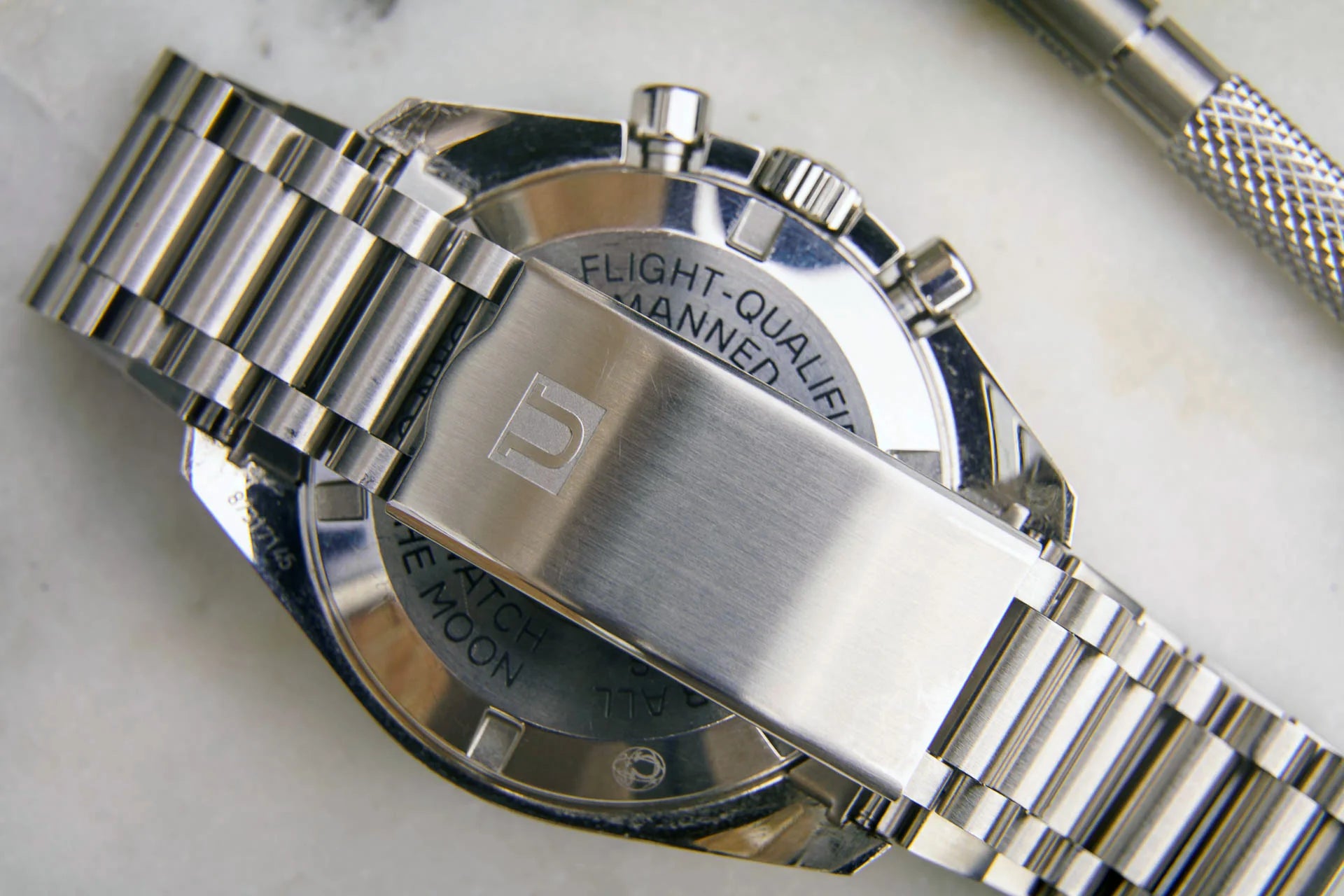 Stainless steel chronograph watch with "Flight-Qualified" text, metal bracelet, and oversized case detail on light background