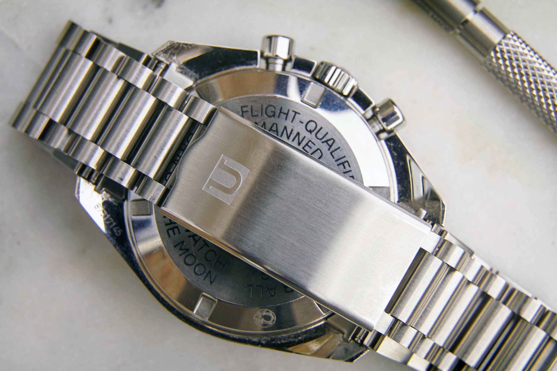 Stainless steel chronograph watch with flight-qualified bracelet and dial text, overhead flat lay view
