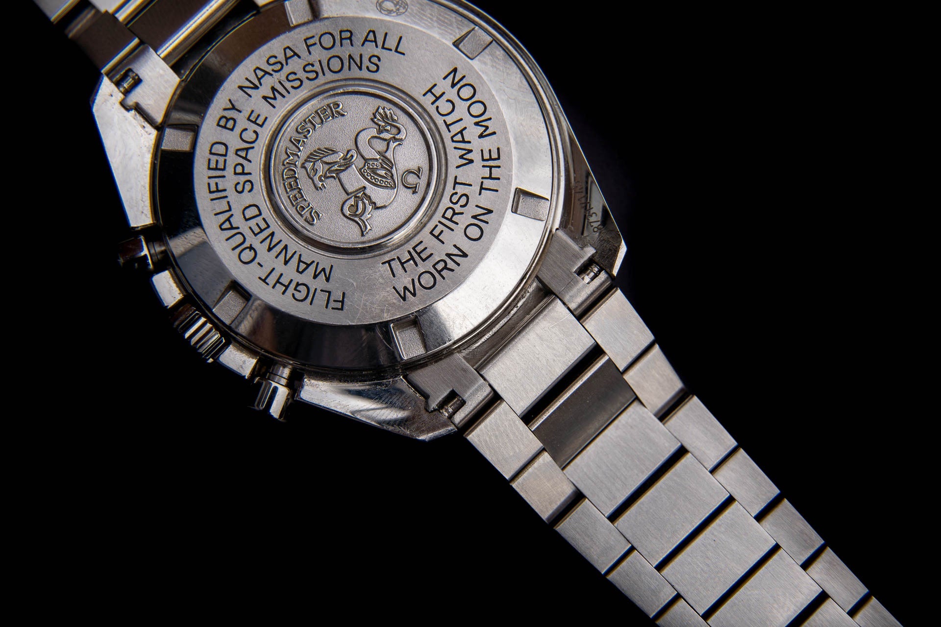 Omega Speedmaster watch with stainless steel bracelet showing engraved case back with NASA space missions logo and text