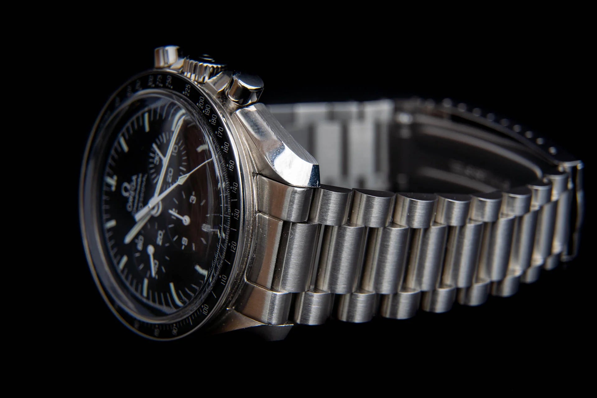 Omega Speedmaster Professional chronograph watch with black dial, stainless steel bracelet and tachymeter bezel on black background