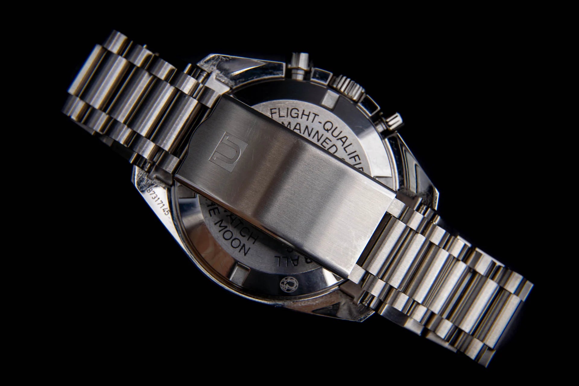Flight-qualified stainless steel chronograph watch with metal bracelet and black dial, rear view showing engraved caseback