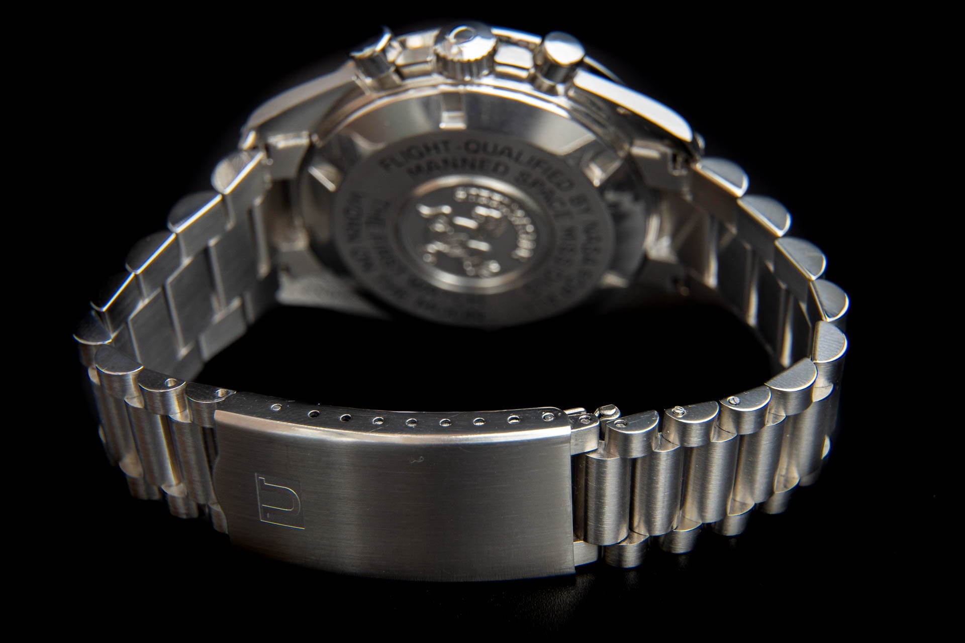 Silver stainless steel chronograph watch with bracelet band shown from rear case back view against black background