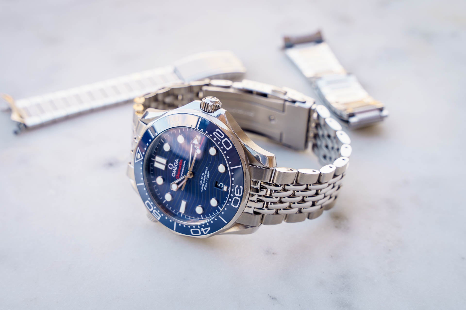 Omega Seamaster 300m dive watch with blue dial, steel bracelet, and extra watch straps displayed on white marble surface
