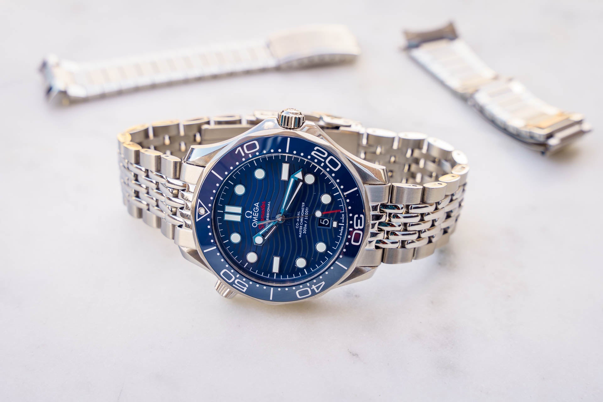 Omega Seamaster 300m diving watch with blue dial, stainless steel bracelet, and interchangeable beads of rice strap options