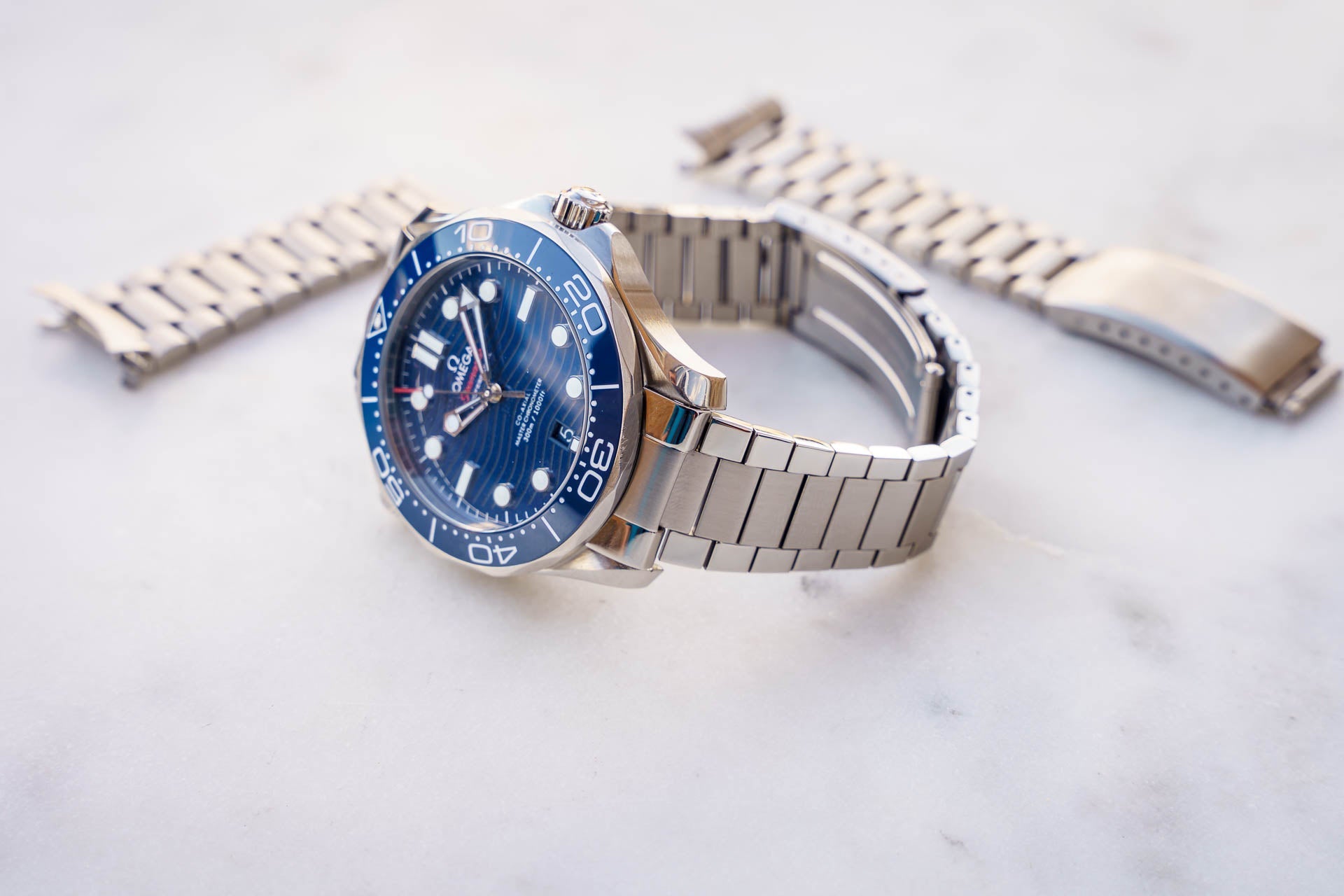Omega Seamaster 300m dive watch with blue dial, stainless steel bracelet and extra link bracelets on white marble background