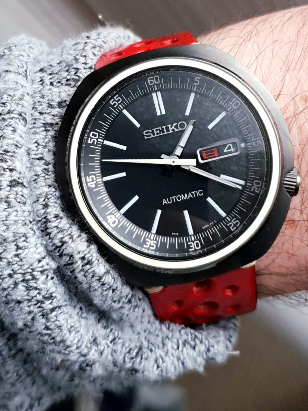 Seiko automatic watch with black dial, white indices, date window, and red rubber rally strap on wrist