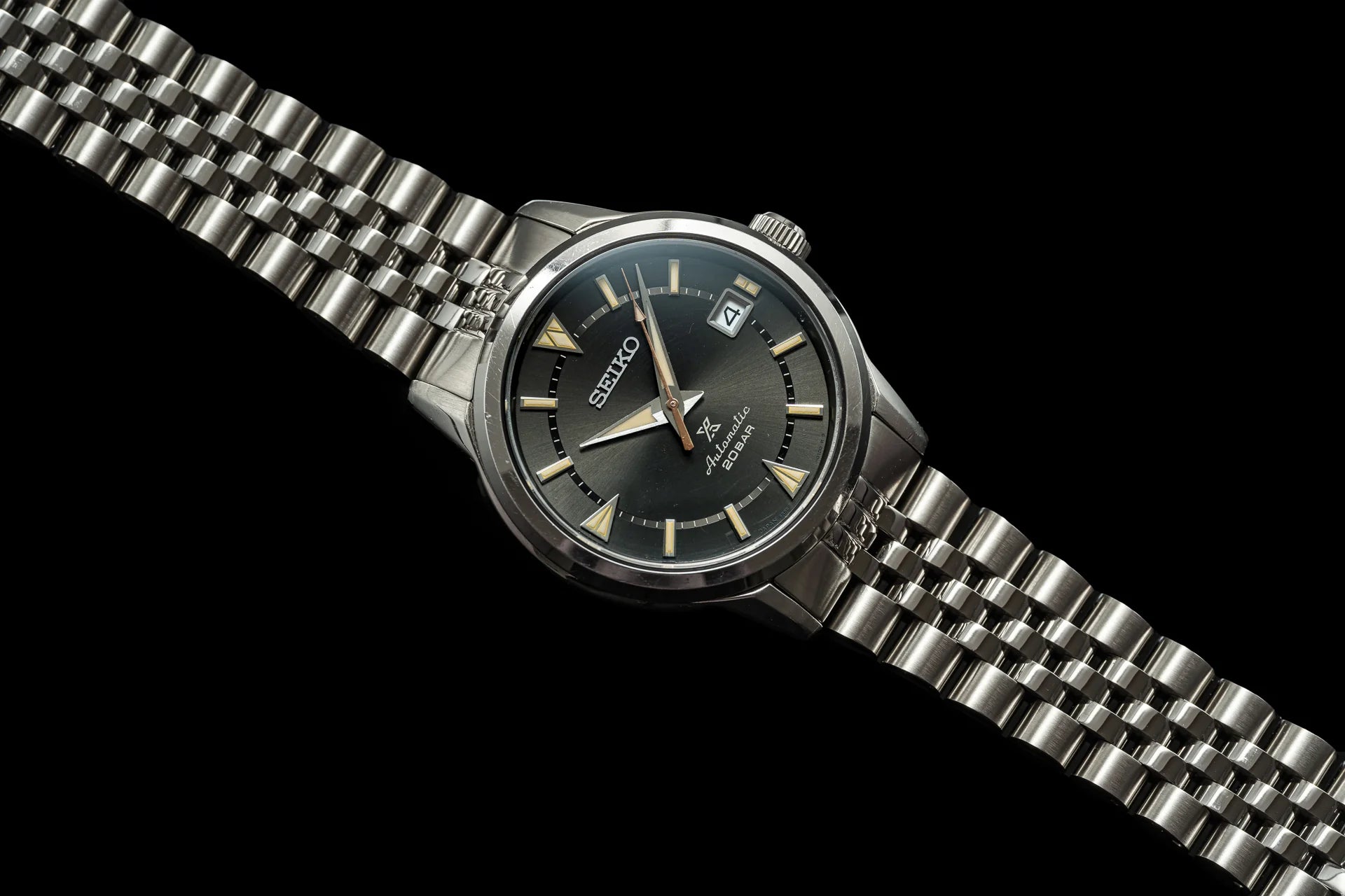 Seiko Alpinist watch with stainless steel bracelet, black dial, gold indices, and date window on black background