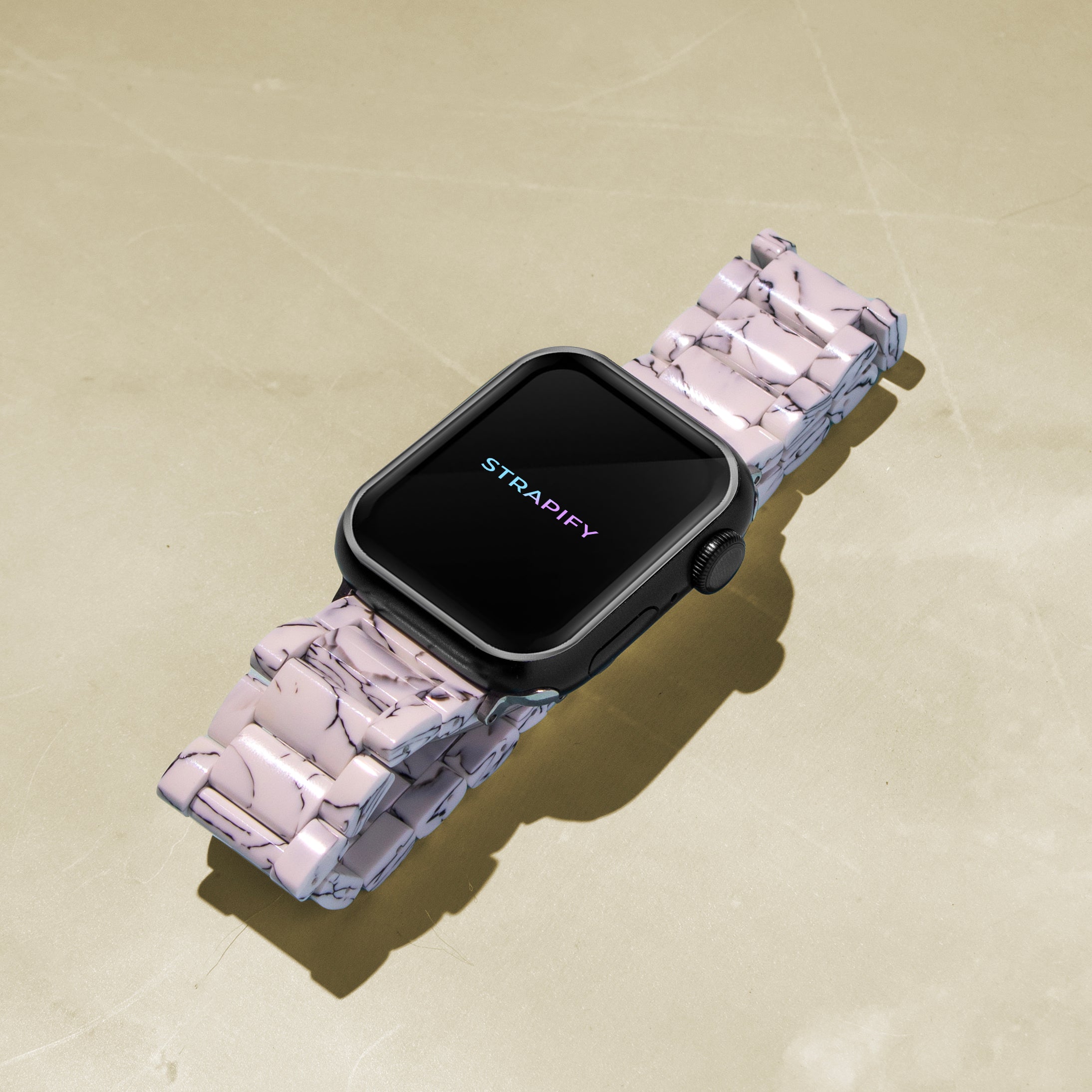Smartwatch with black square face and pink marble patterned acetate band on beige background, displaying Strapify branding