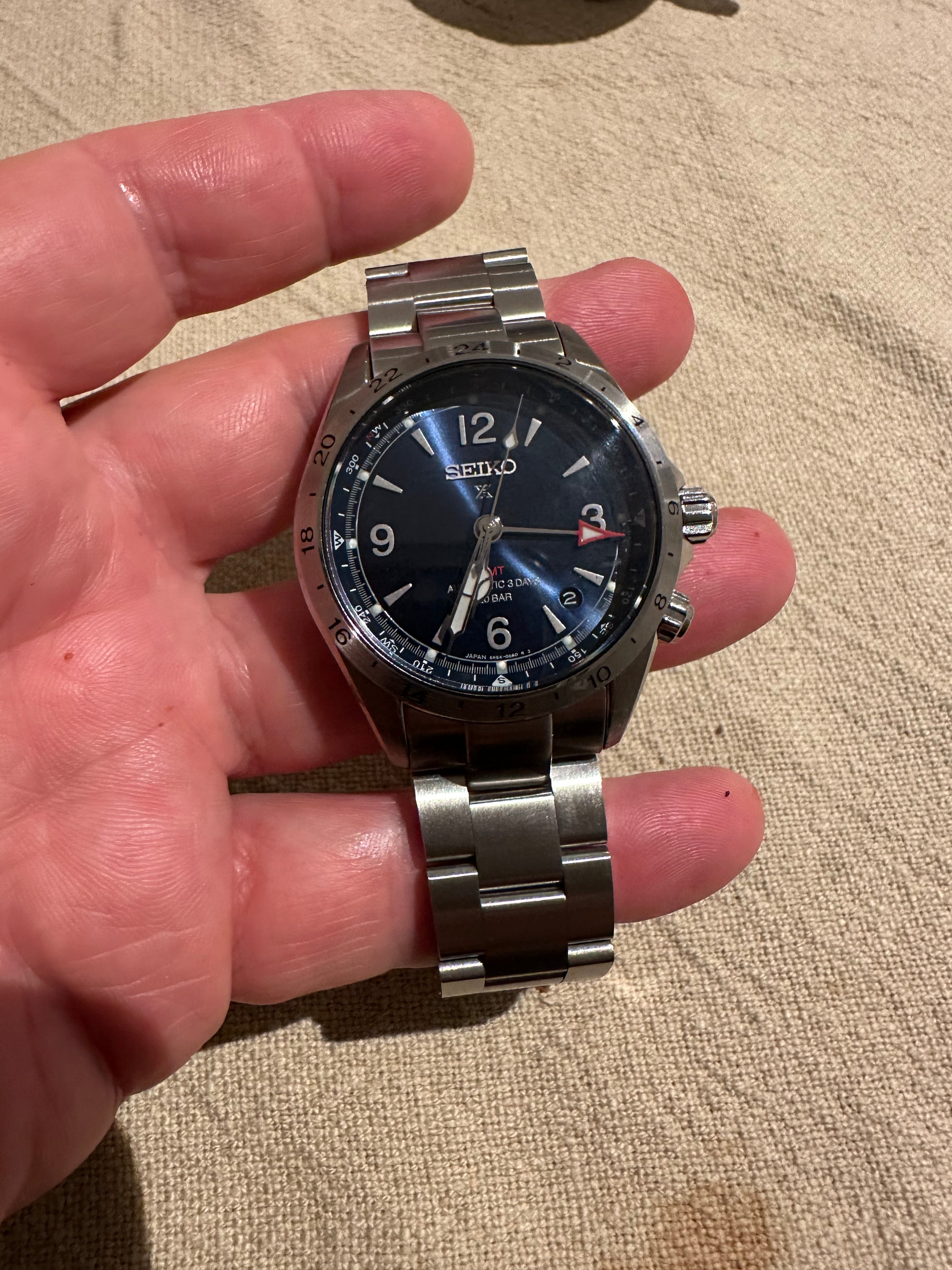 Seiko Prospex stainless steel watch with black dial held in hand, showing 3 o'clock position and metal bracelet