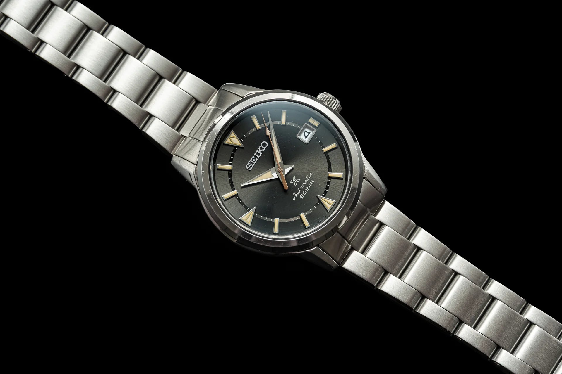Seiko Alpinist automatic watch with stainless steel bracelet, black dial, date window, and gold hour markers on black background