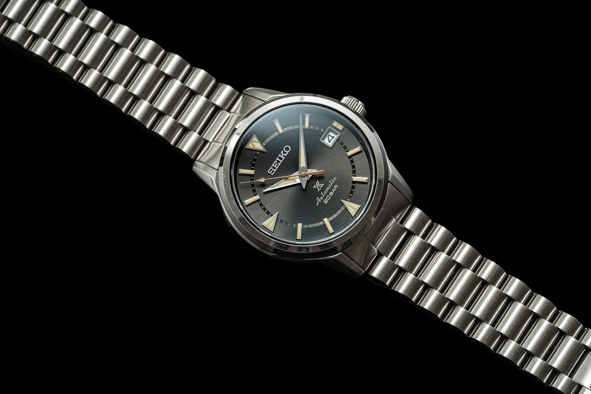 Seiko Alpinist automatic watch with stainless steel bracelet, black dial, gold hour markers and date window on black background
