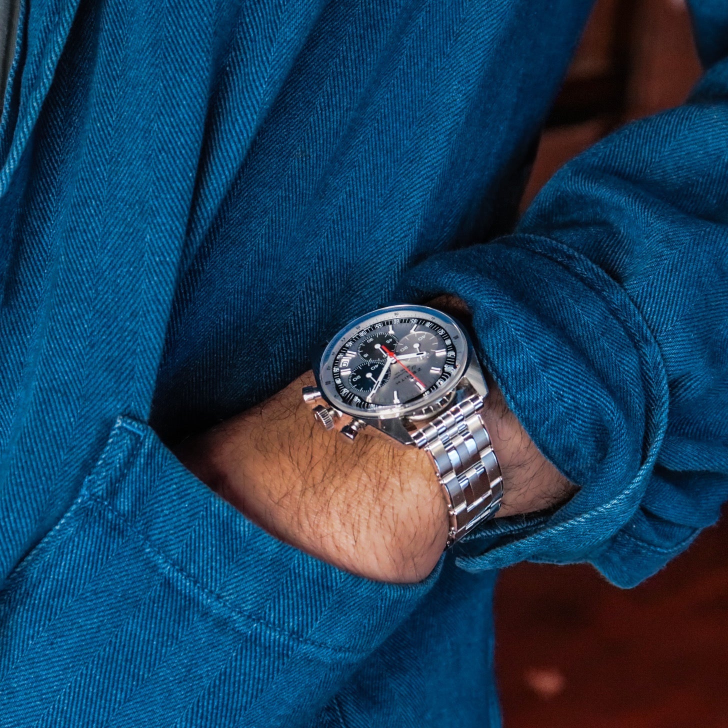 Stainless steel chronograph watch with black dial on man's wrist wearing blue textured jacket