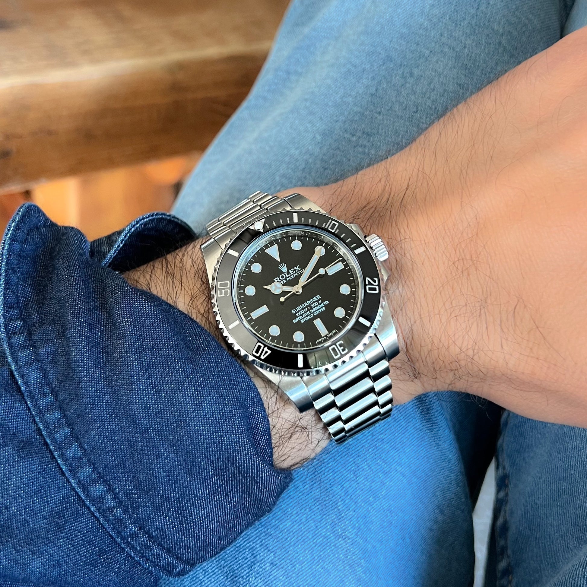 Stainless steel Rolex Submariner watch with black dial on wrist wearing blue denim