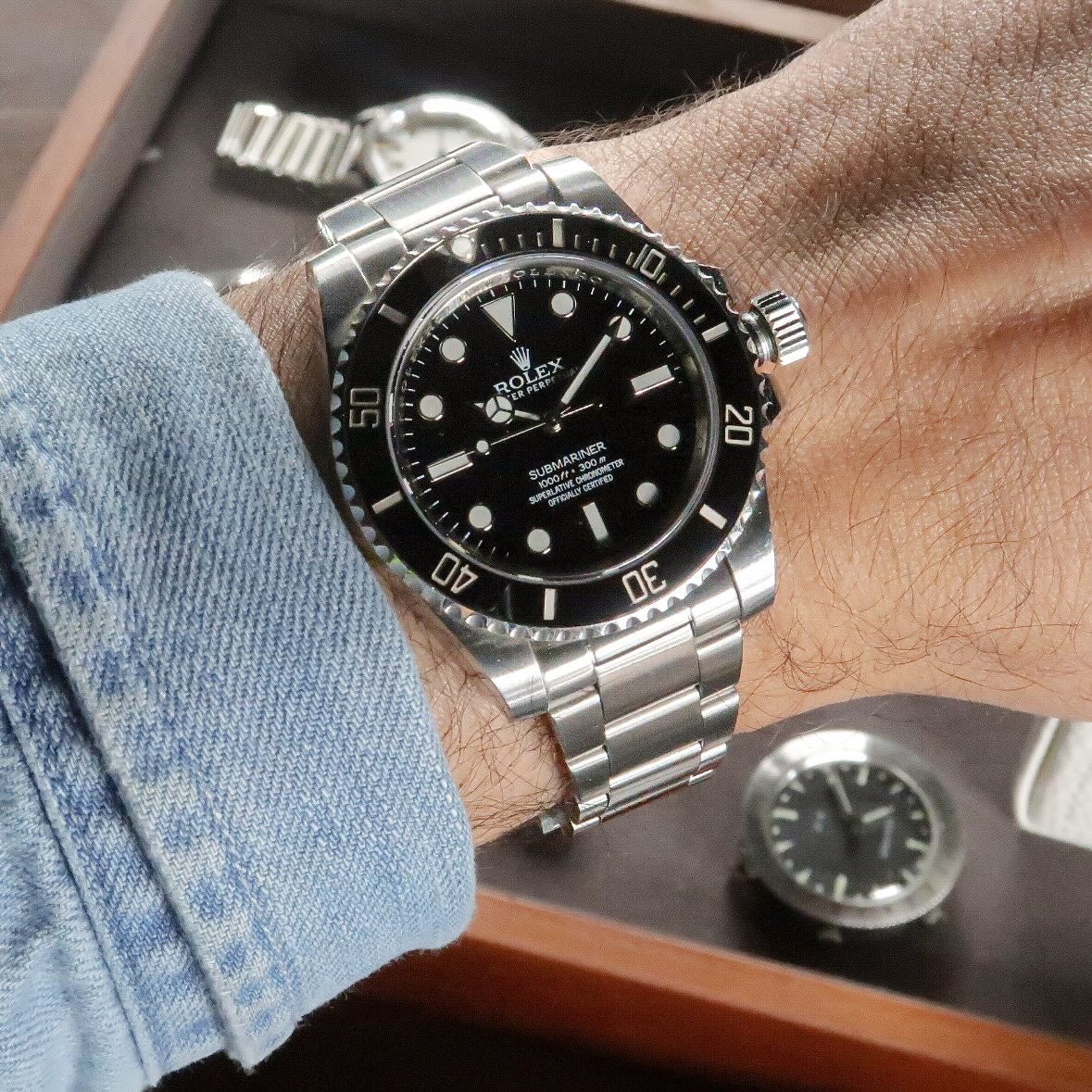 Rolex Submariner stainless steel watch with black dial and rotating bezel worn on wrist with blue shirt sleeve