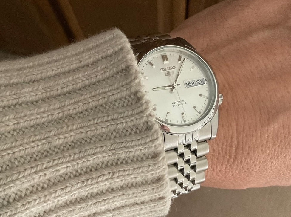 Seiko 5 SNKL automatic watch with silver stainless steel bracelet and white dial worn on wrist with cream sweater