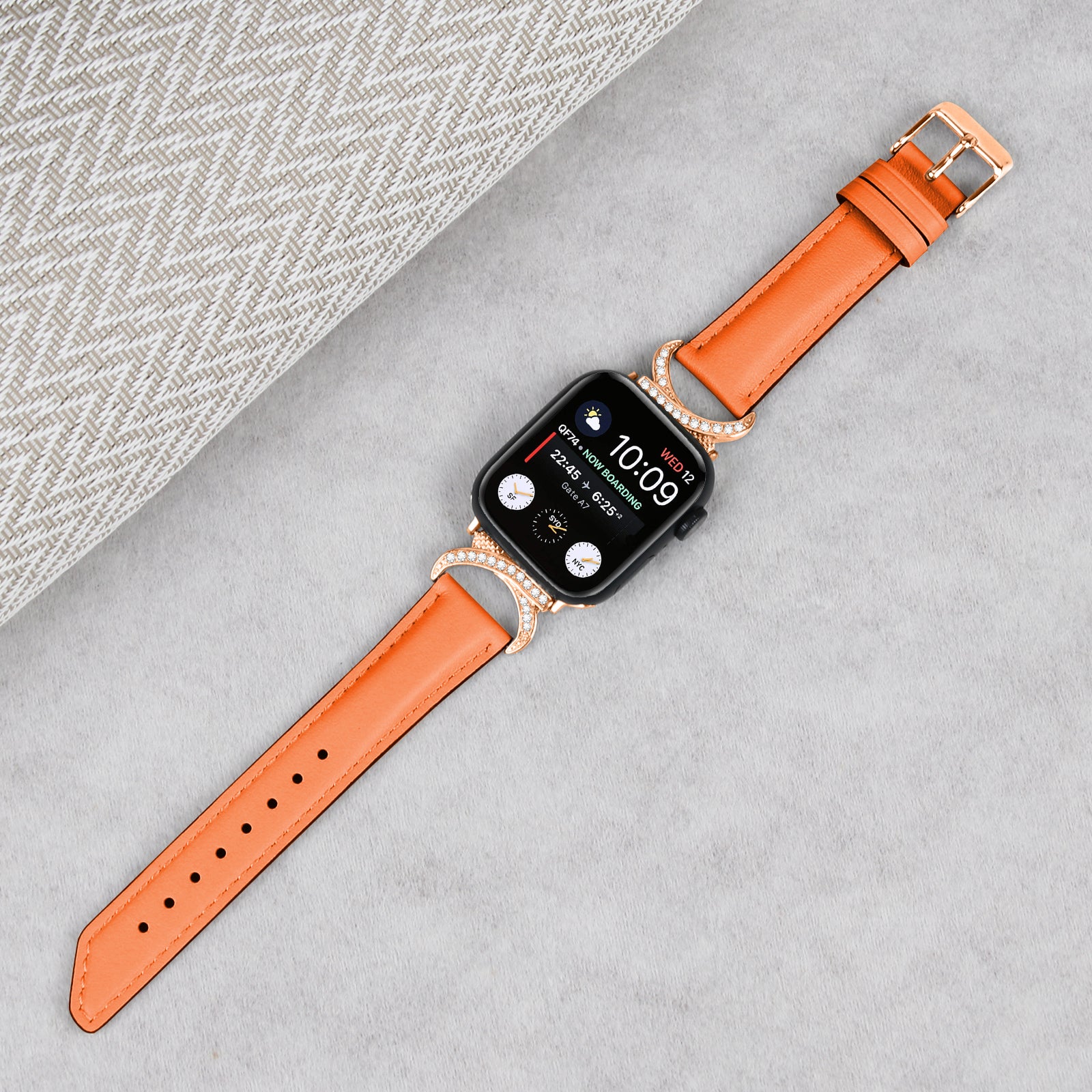 Apple Watch with orange leather band and rose gold diamond-studded case displaying time on black screen