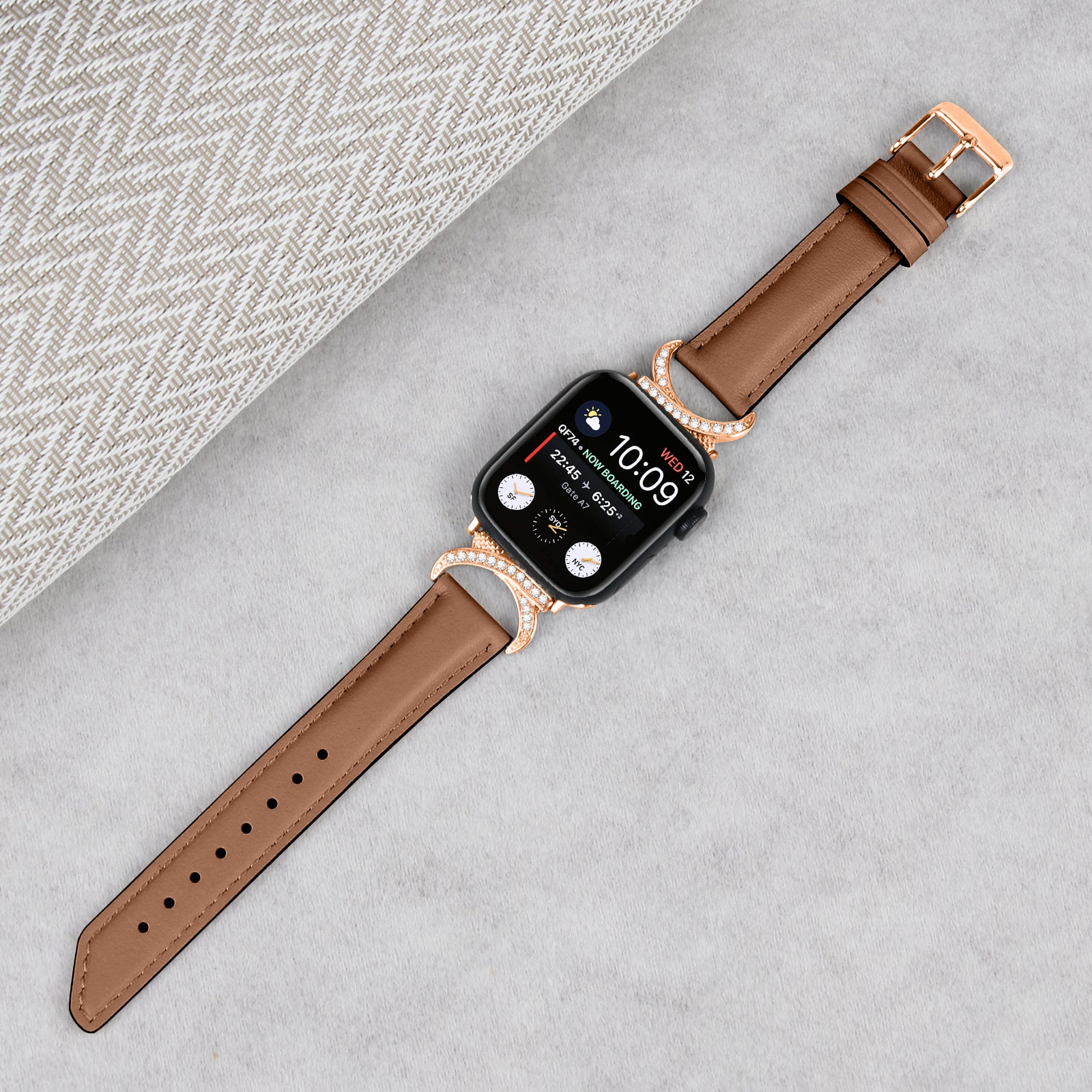 Rose gold smartwatch with black case and tan leather band, featuring crystal-embellished connectors on gray background