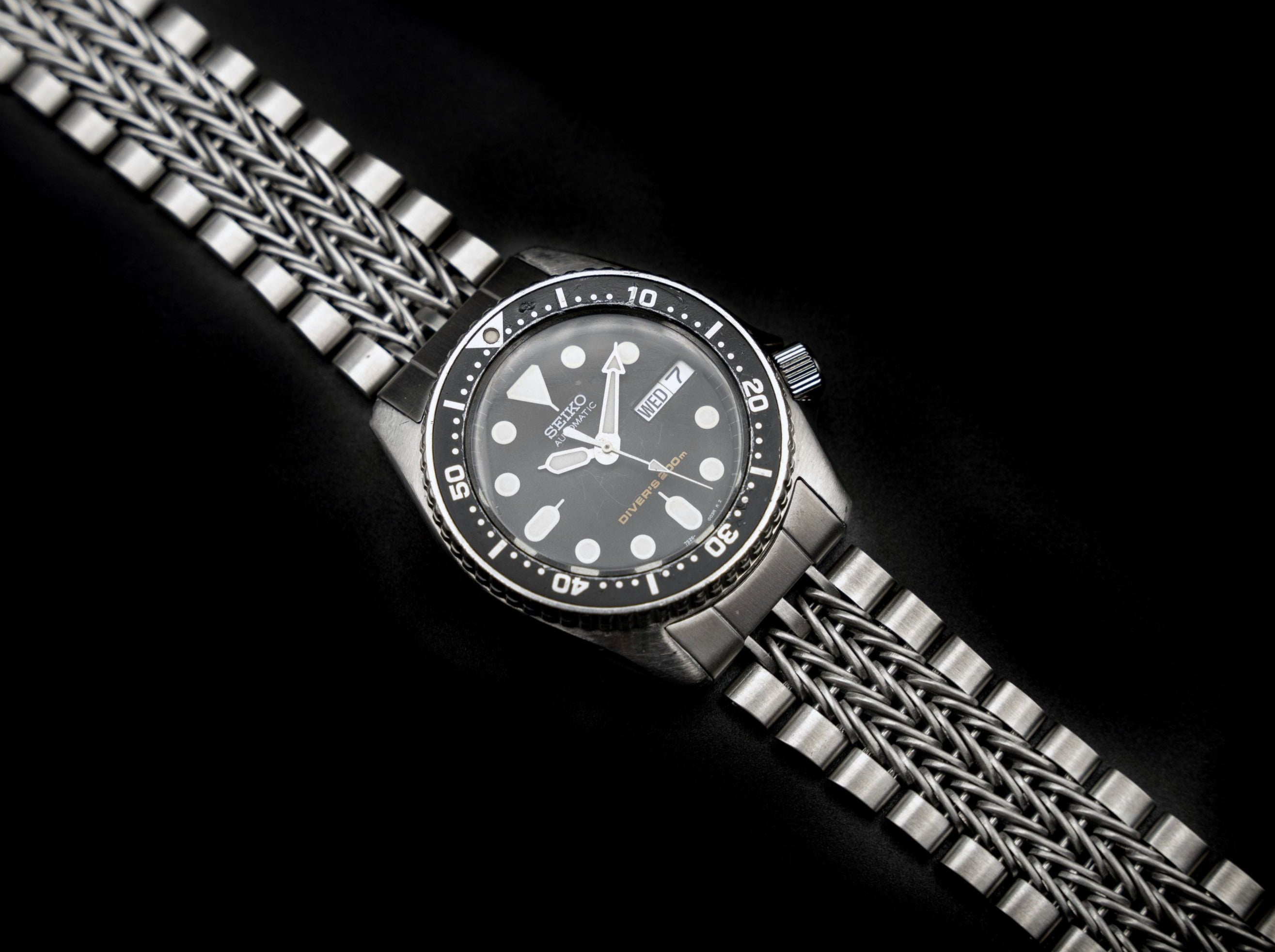 Seiko SKX013 dive watch with black dial, luminous markers, and stainless steel bracelet on black background