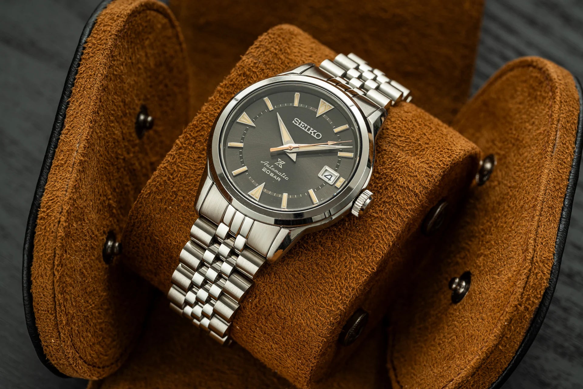 Seiko Alpinist stainless steel watch with dark dial and gold indices on tan suede display stand