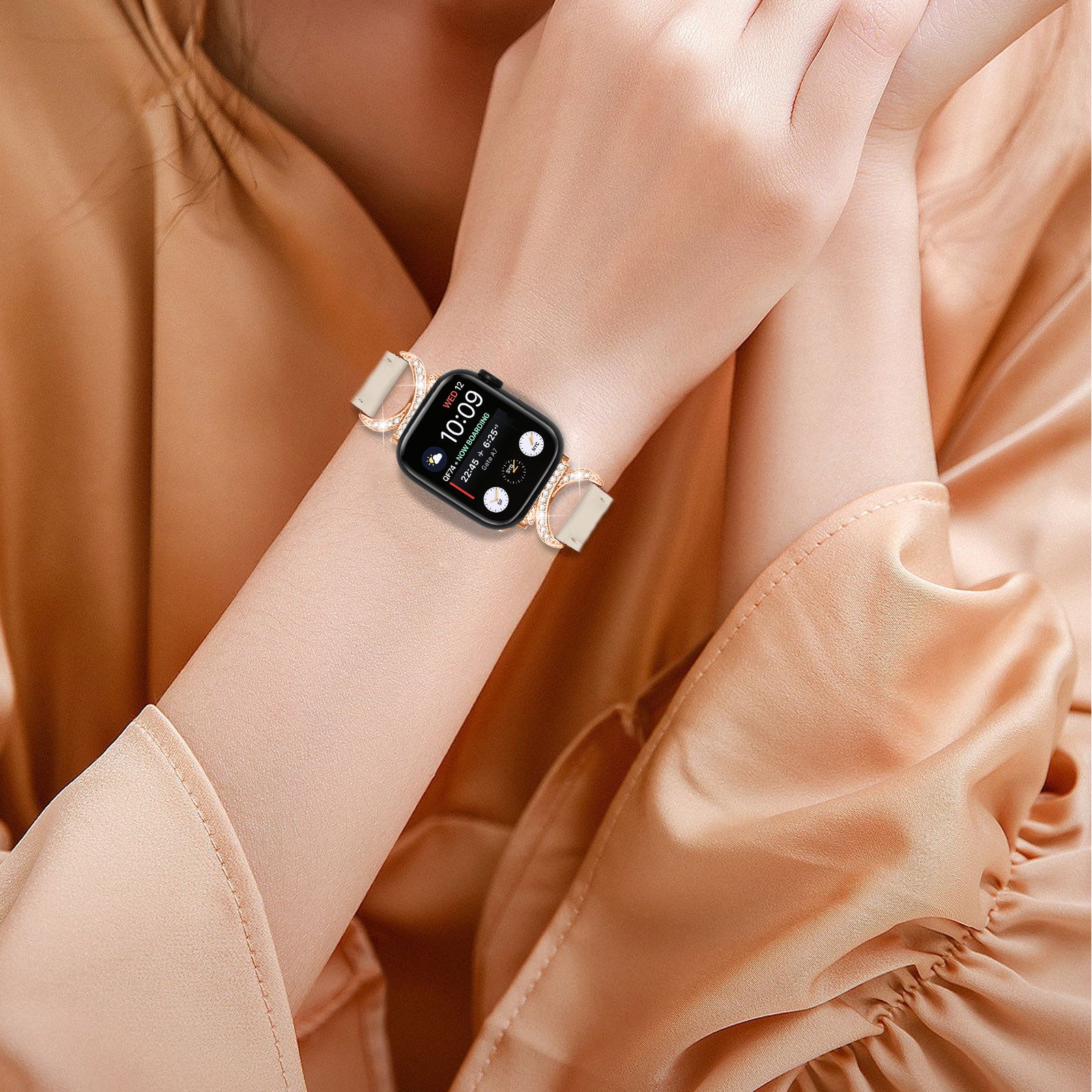 Smartwatch with black square face and champagne leather link band on woman's wrist wearing peach blouse, displaying time 10:09