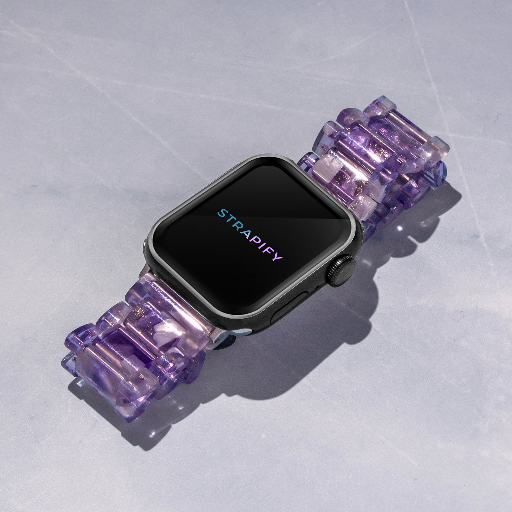 Smartwatch with black display and gunmetal case paired with purple translucent crystalline resin band on white background