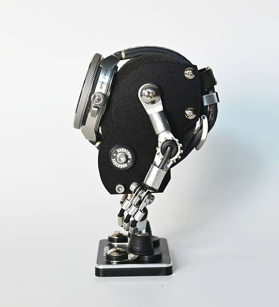 Black robotic watch stand with articulated metal arms and chrome details, displaying timepiece on sculptural base