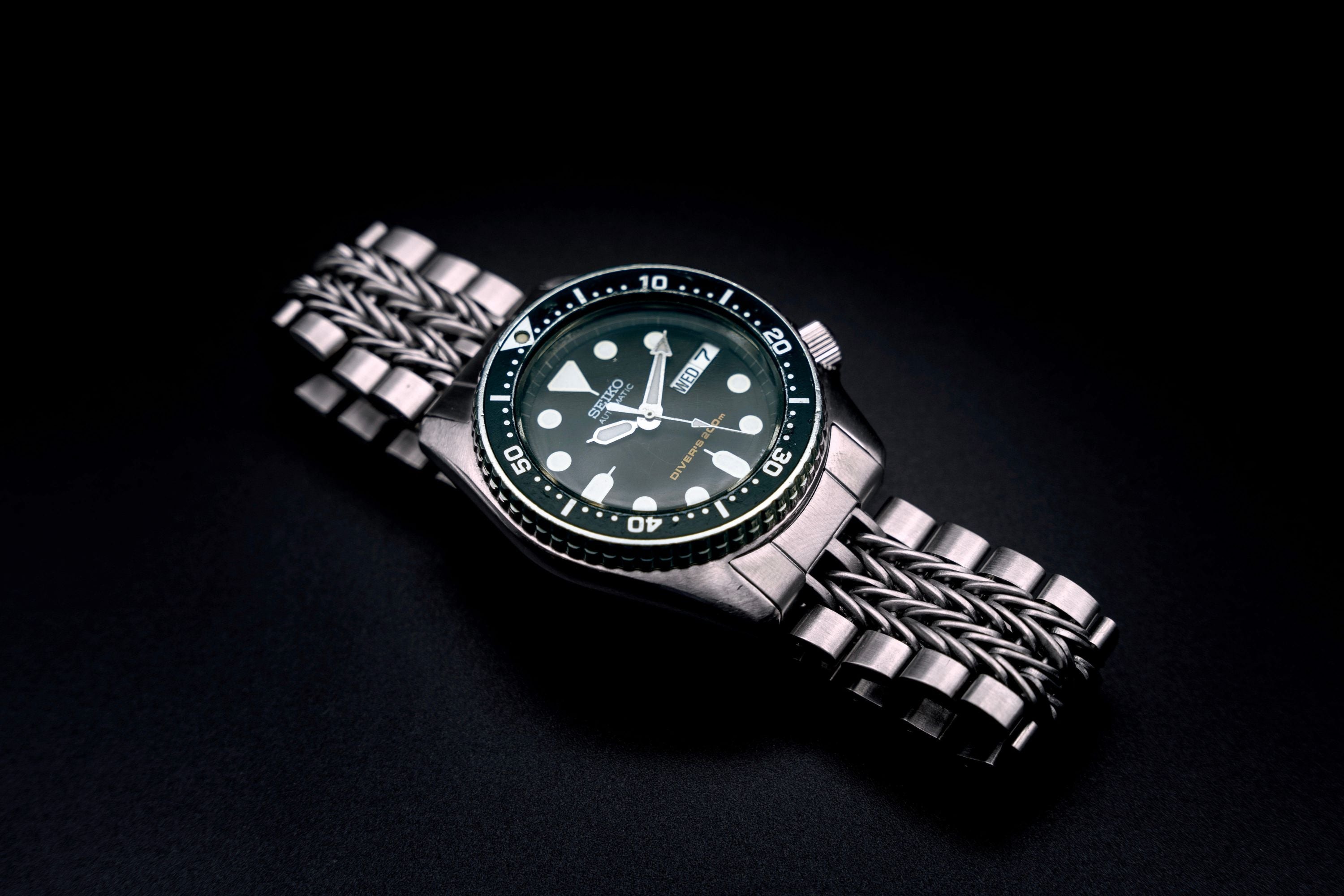 Seiko SKX013 stainless steel dive watch with black dial and razor-wire bracelet on dark background