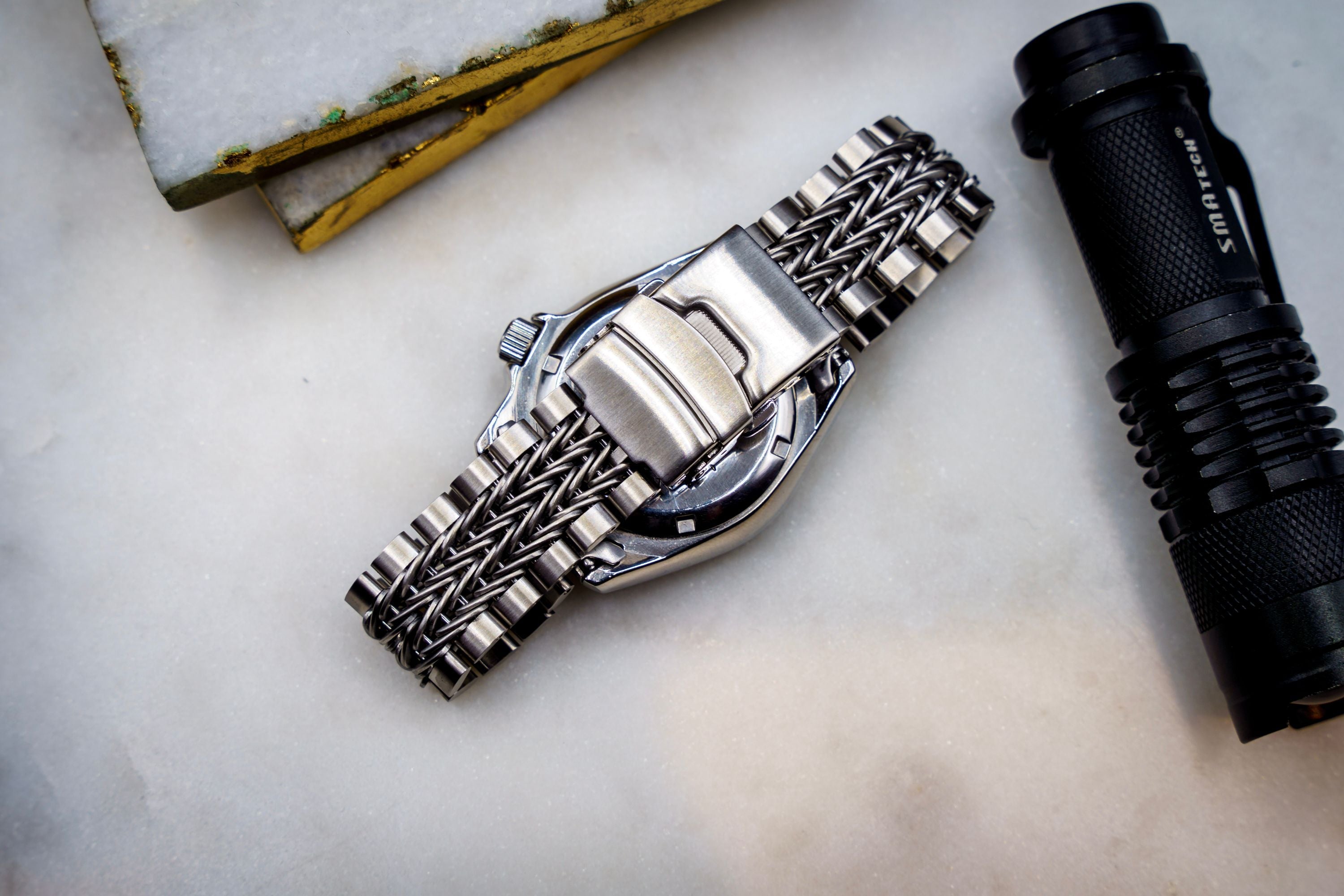 Stainless steel Seiko SKX013 dive watch with razor-wire bracelet displayed alongside tactical flashlight and weathered level