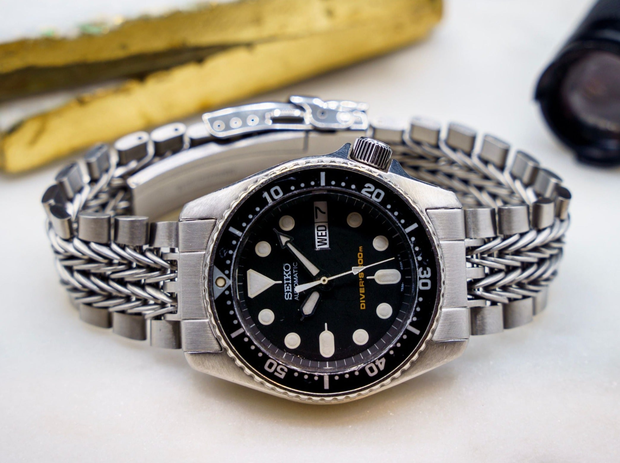 Seiko SKX013 automatic diver watch with black dial, stainless steel bracelet and rotating bezel on white surface with bananas