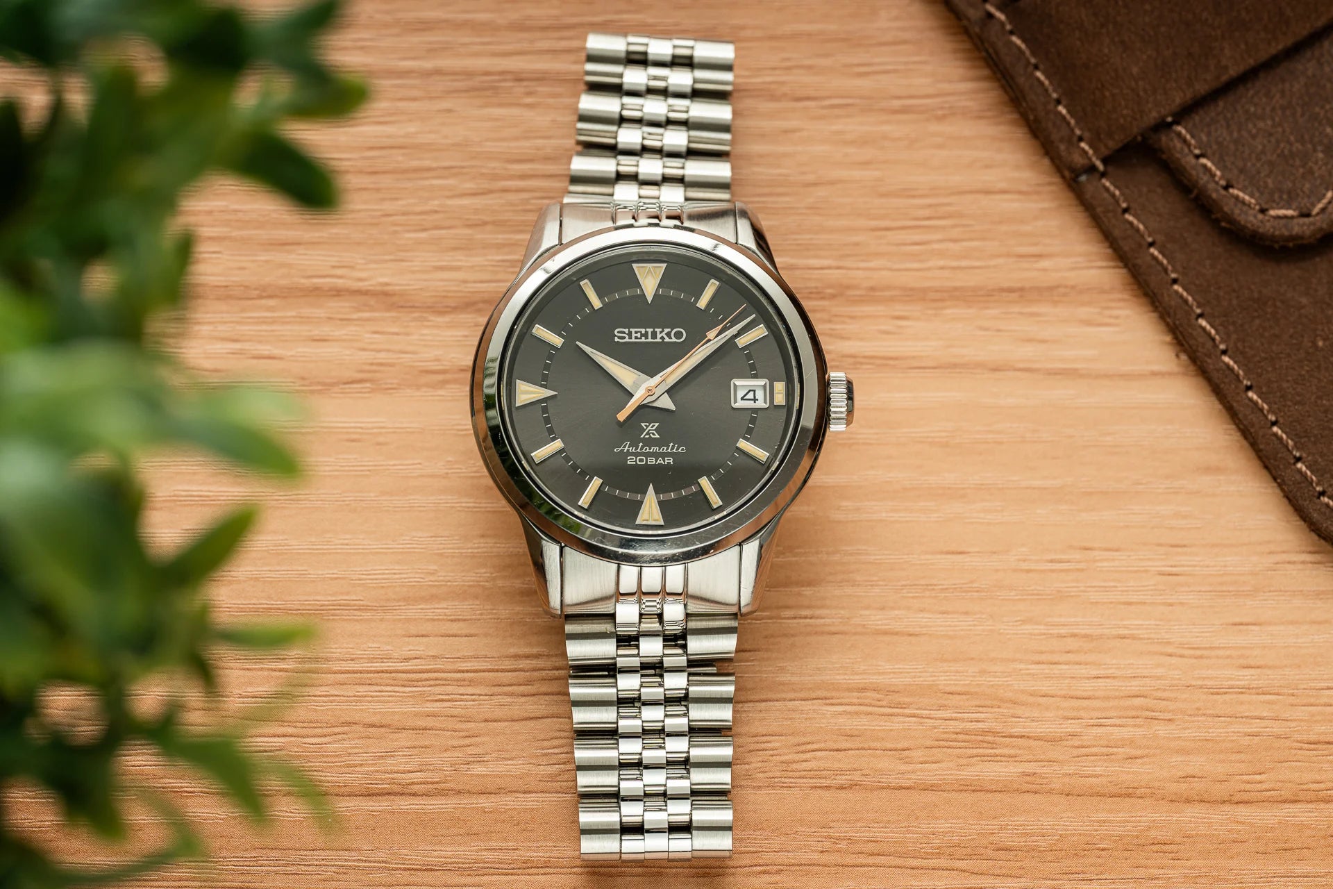Seiko Alpinist automatic watch with charcoal dial, stainless steel bracelet and date window on wooden surface