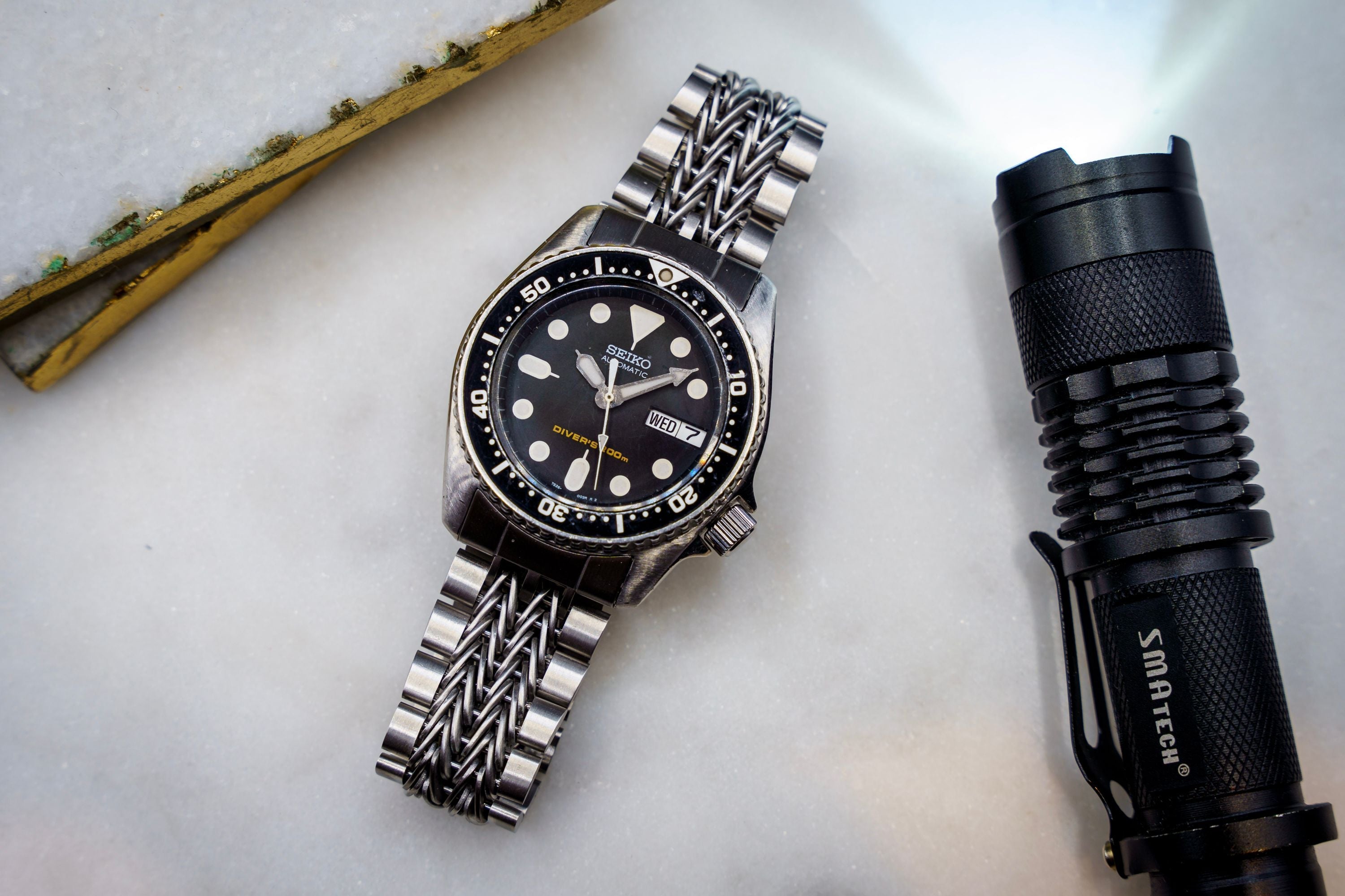 Seiko SKX013 diver watch with stainless steel bracelet and black dial, displayed with tactical flashlight