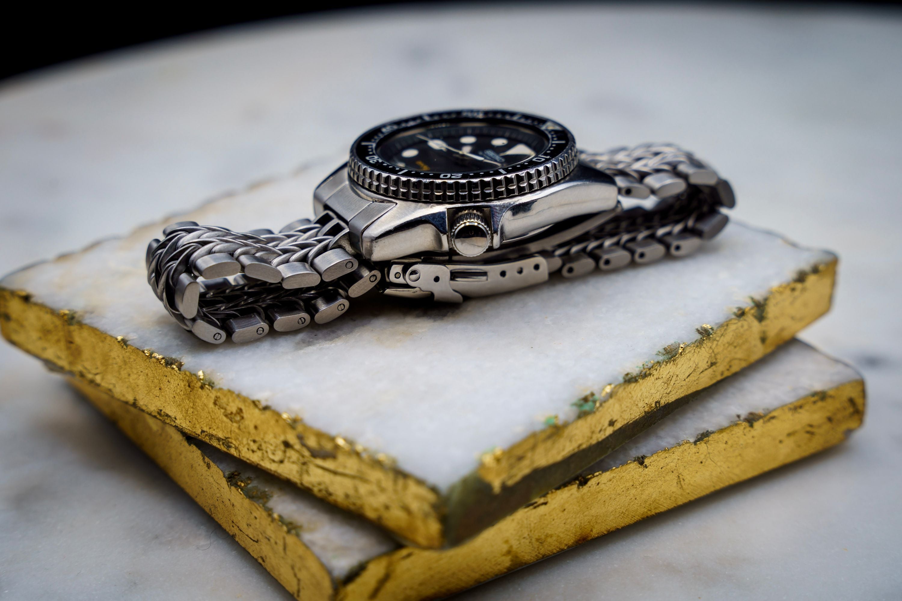 Stainless steel dive watch with black dial and razor-wire metal bracelet on yellow and white wooden display stand