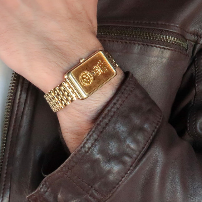 Gold plated Forstner 7-row beads of rice watch bracelet with rectangular gold face on wrist wearing brown leather jacket