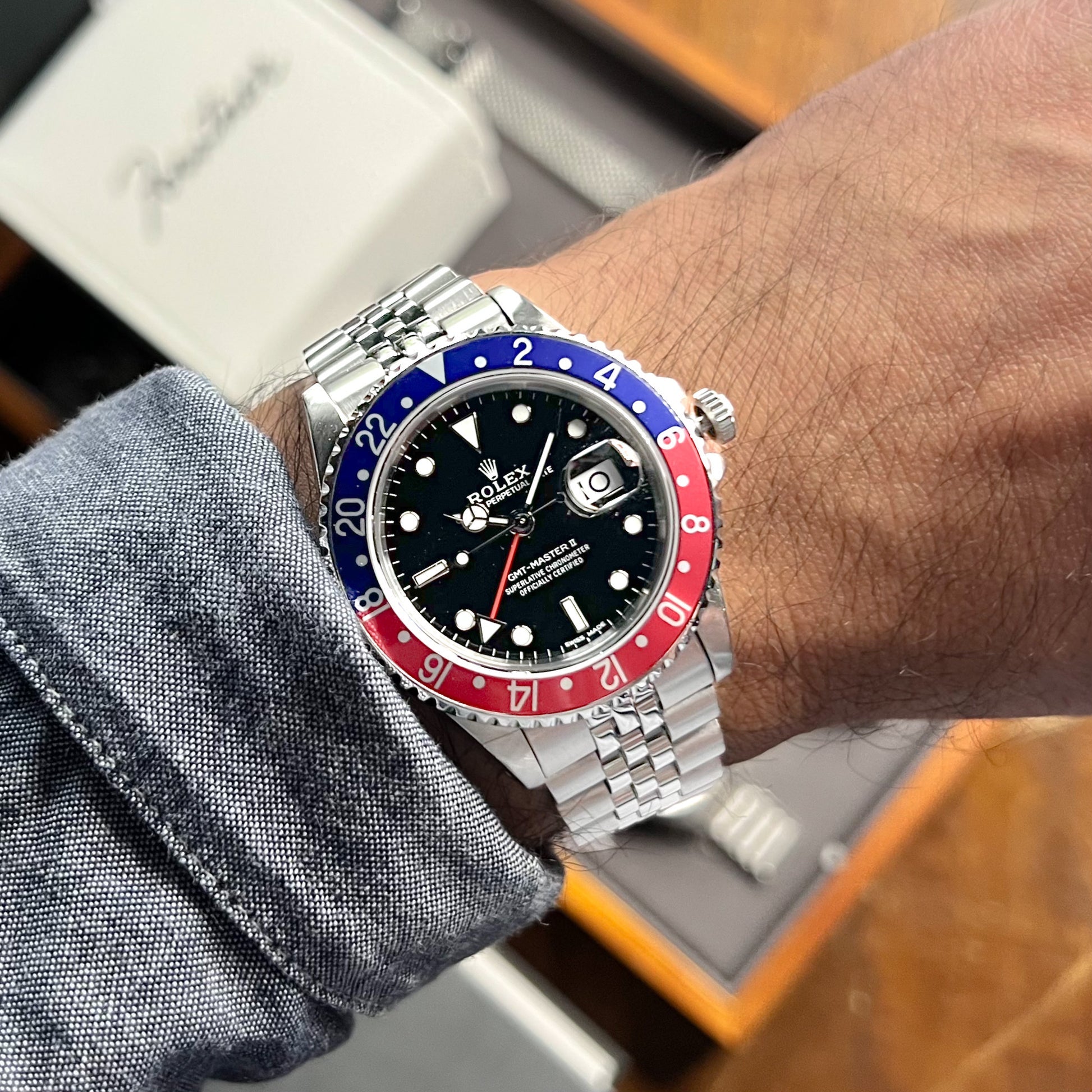 Silver stainless steel watch with black dial, blue and red GMT bezel, worn on wrist with blue fabric cuff