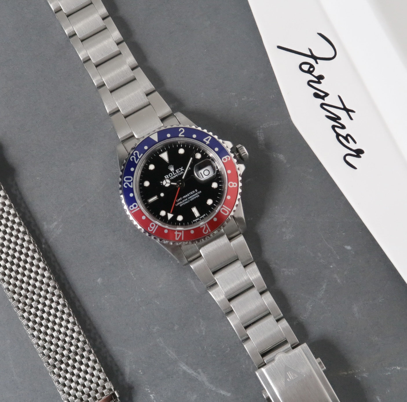 Stainless steel Rolex GMT-Master II watch with black dial, blue and red bezel, and metal bracelet on gray surface