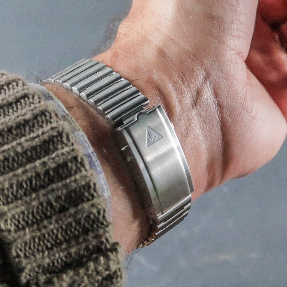 Stainless steel barrel bracelet with ribbed links worn on wrist with beige knit sleeve