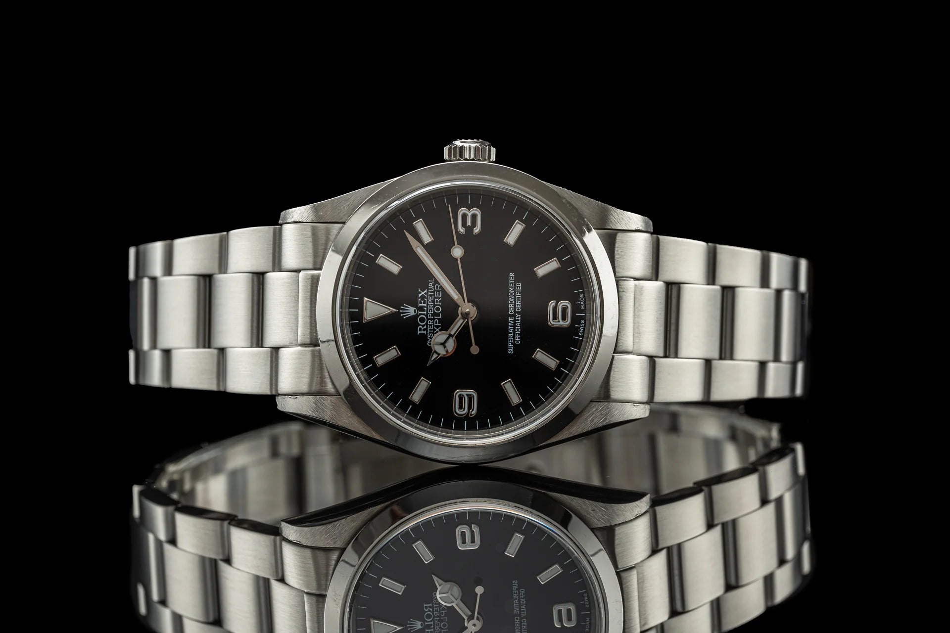 Stainless steel Rolex Explorer watch with black dial and bracelet, shown from front angle on reflective black surface