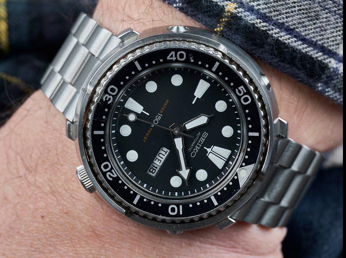 Men's stainless steel dive watch with black dial, luminous markers, rotating bezel, and matching metal bracelet on wrist