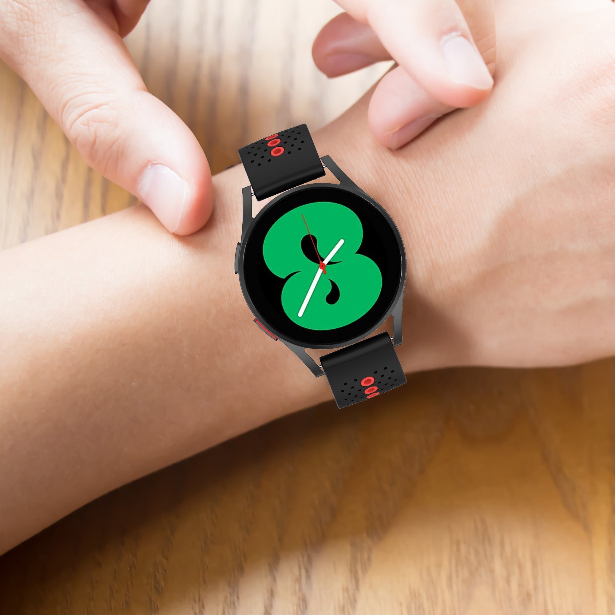 Black sports smartwatch with green face and perforated silicone strap, worn on wrist showing quick release band detail
