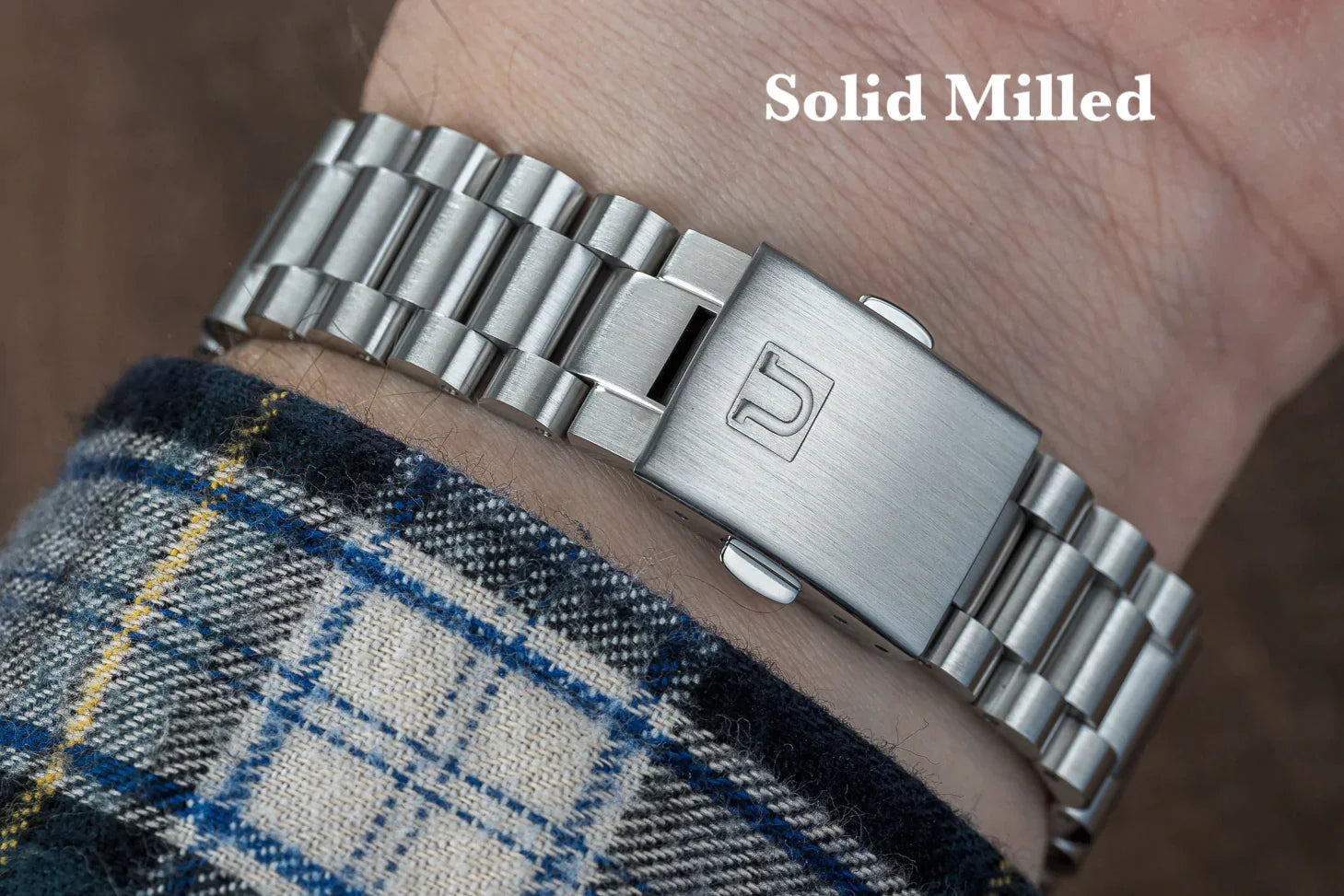 Silver solid milled bracelet with rectangular links and numbered clasp worn on wrist with plaid fabric cuff