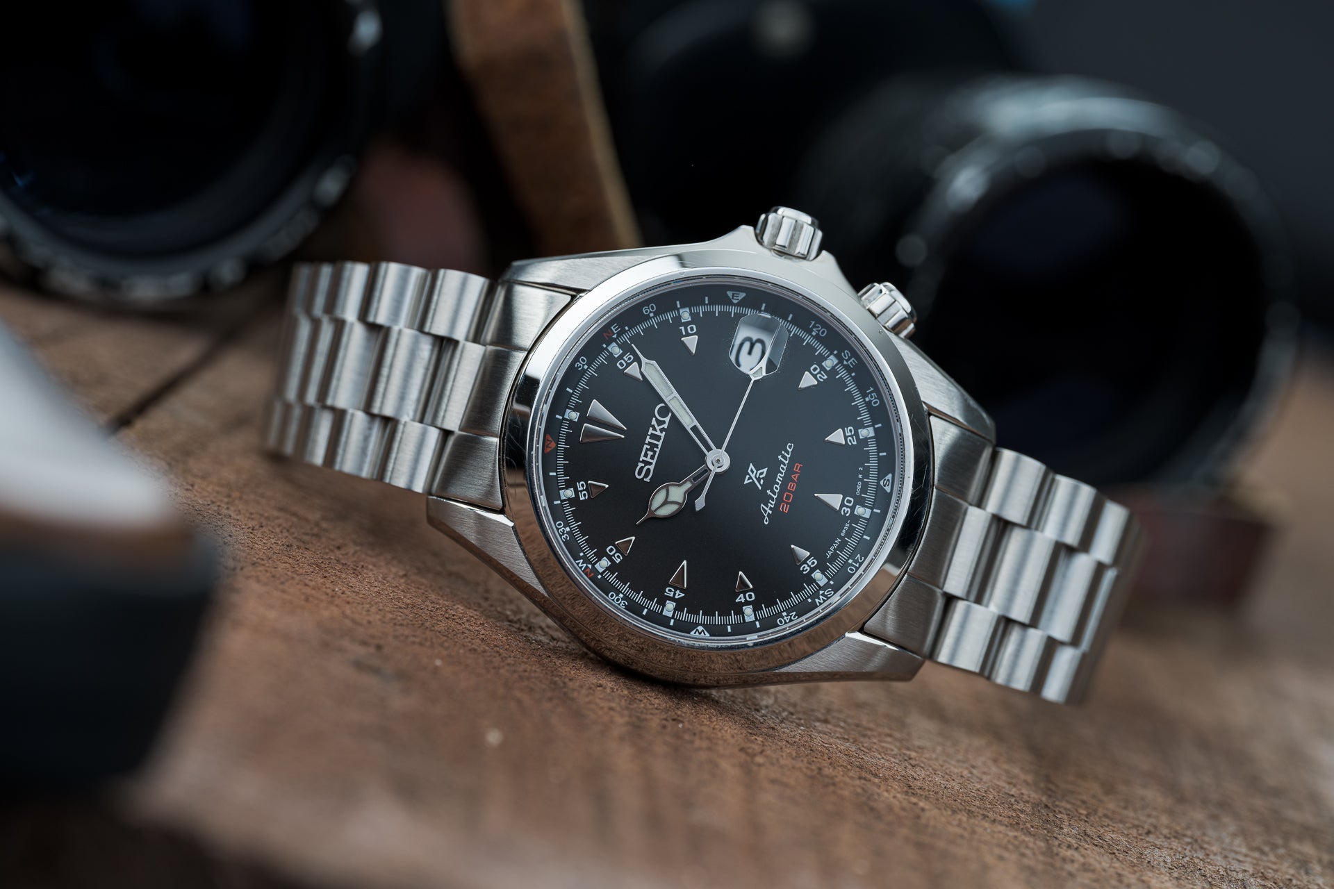 Seiko Alpinist SARB017 stainless steel chronograph watch with black dial and metal bracelet on wooden surface