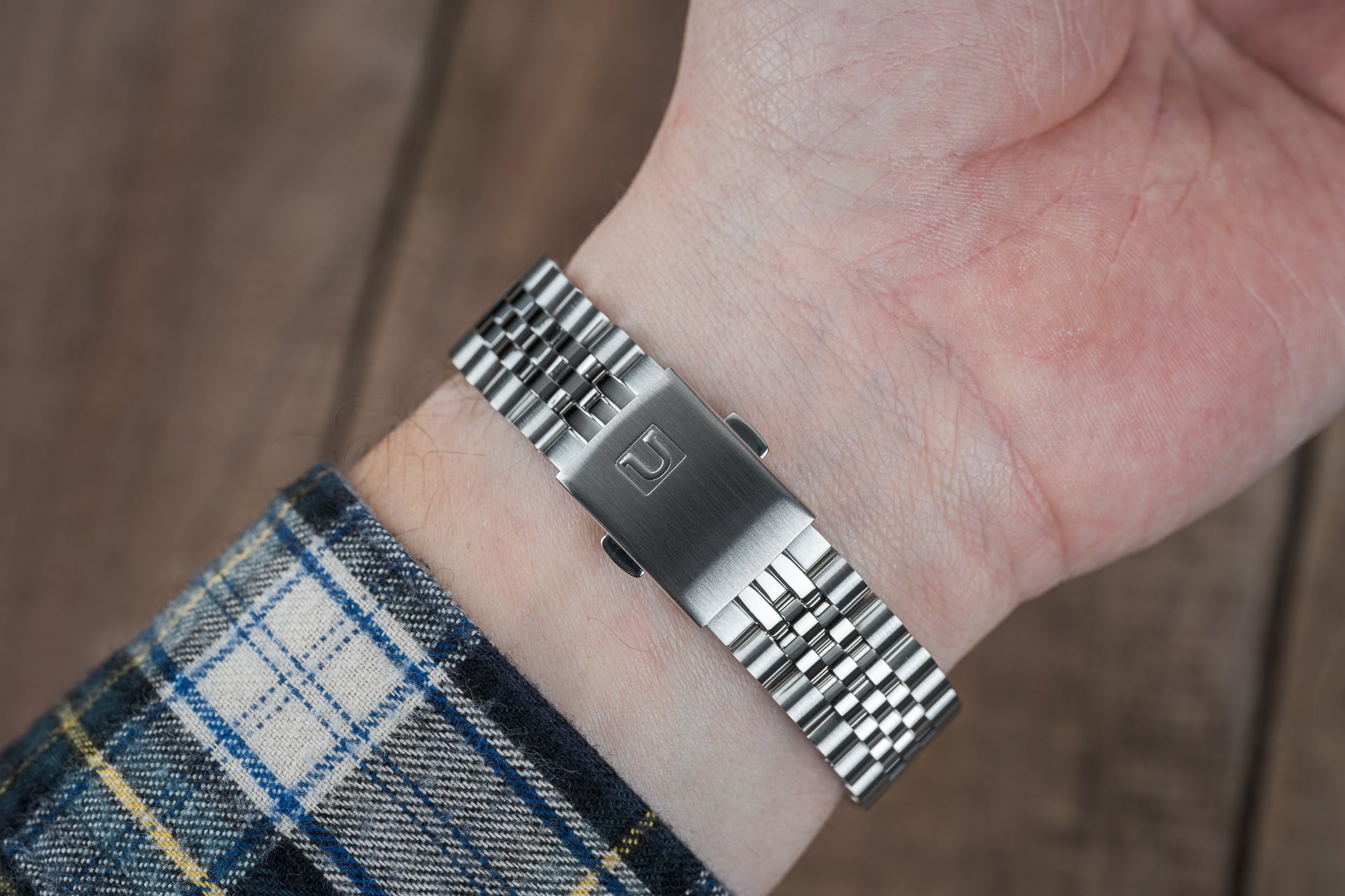 Stainless steel executive bracelet with brushed center link and polished end links worn on wrist with plaid shirt sleeve