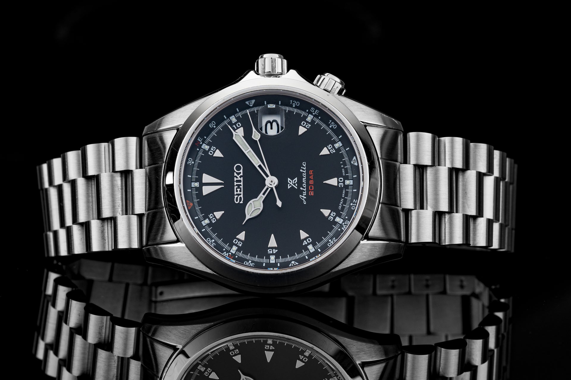 Seiko Alpinist SARB017 stainless steel watch with black dial, white hour markers, and matching metal bracelet on black background