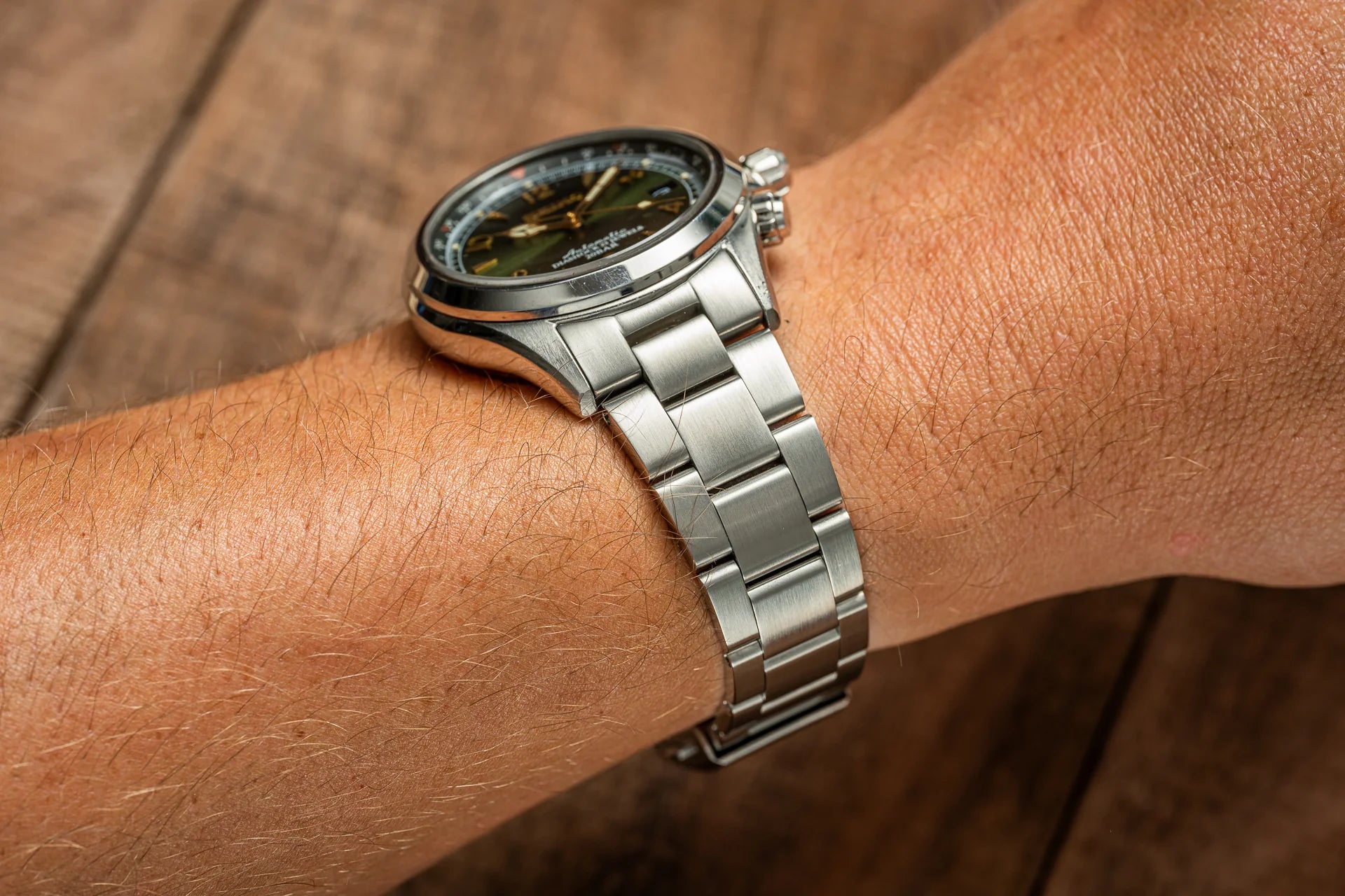 Men's stainless steel watch with olive dial and metal bracelet on wrist, showcasing classic timepiece design