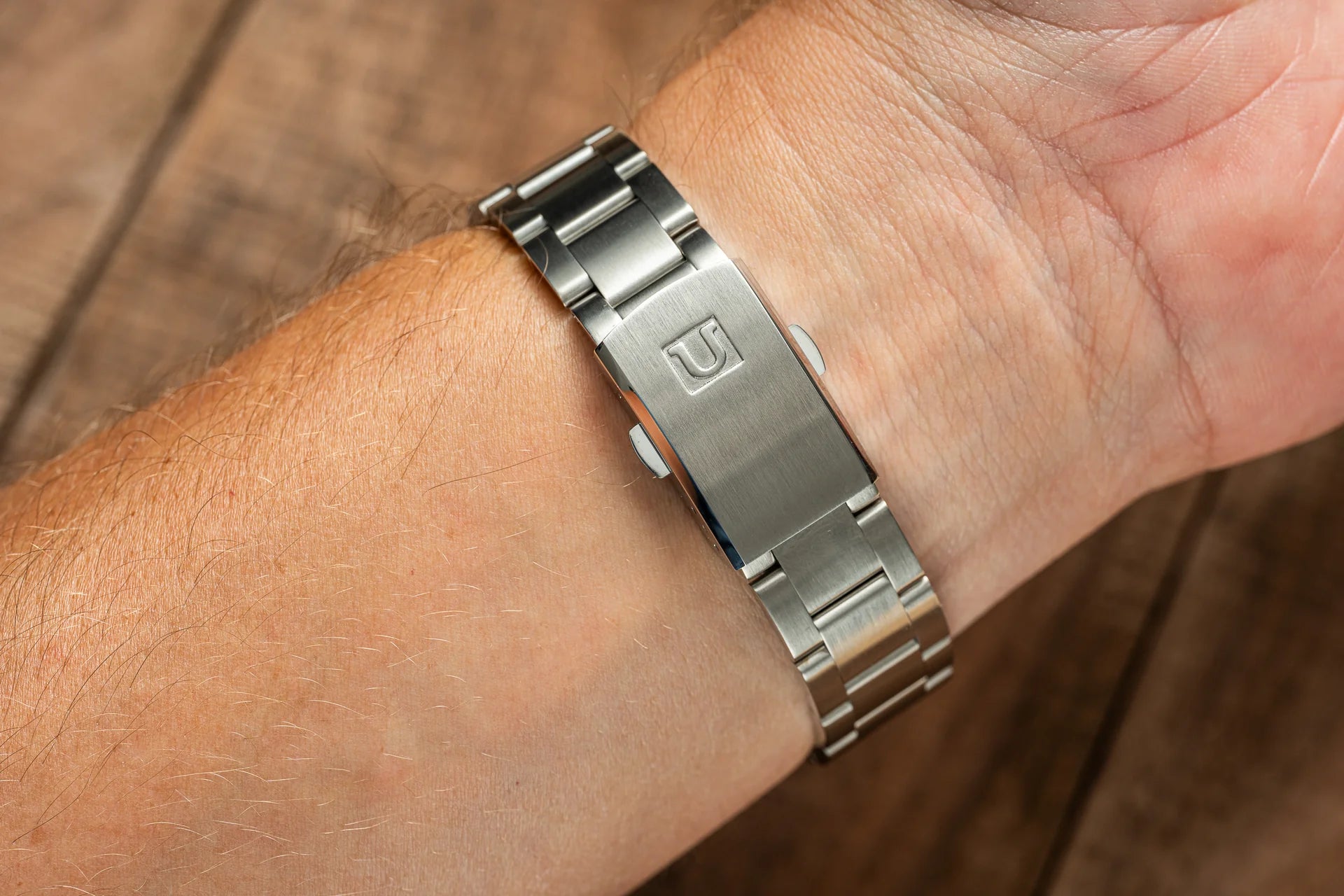 Stainless steel watch bracelet worn on wrist, featuring brushed metal links and engraved clasp, classic dress watch band style